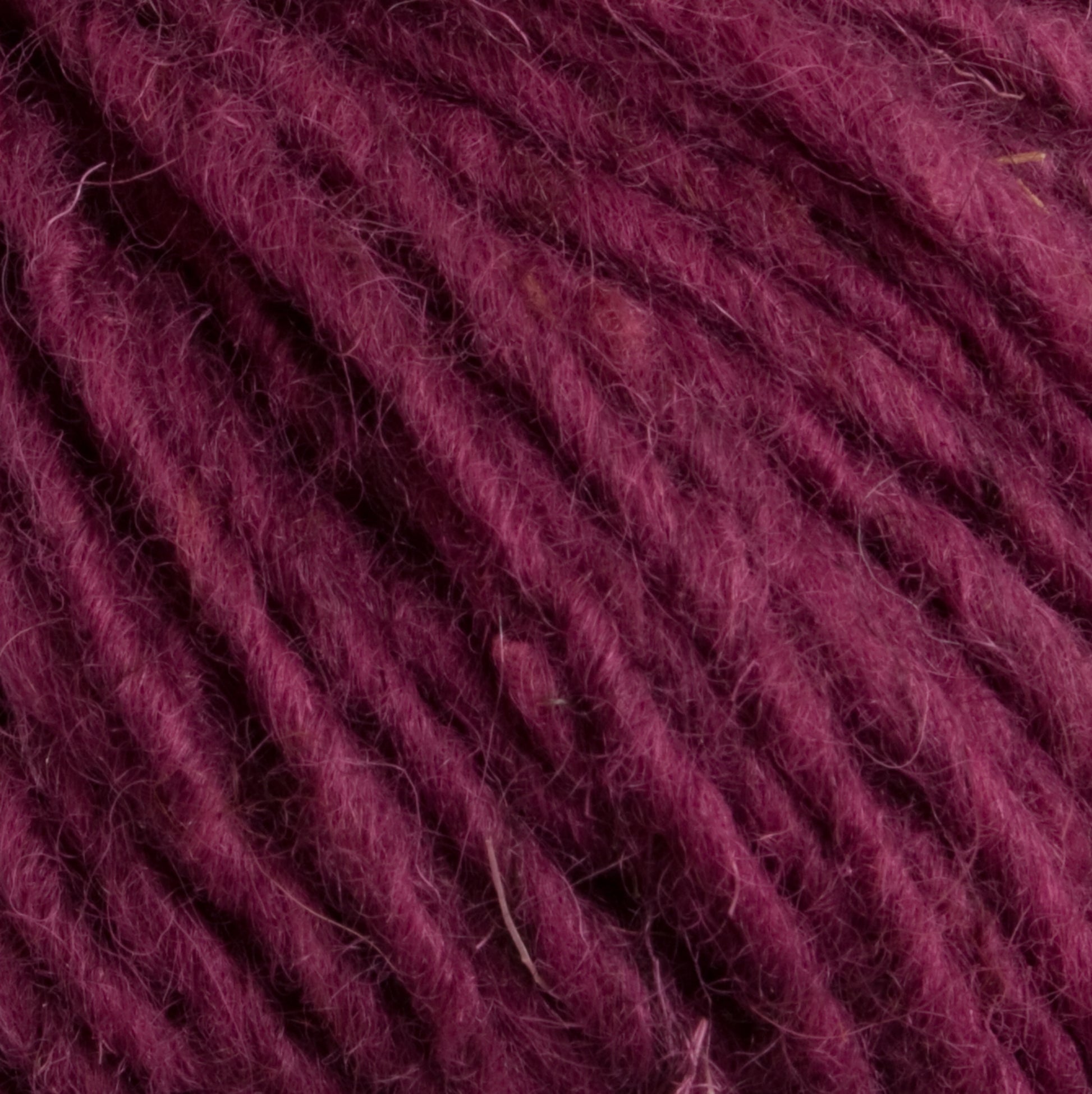 Close-up image of soft, burgundy-colored Caledonian Dye Works Halcyon Geo Rug Wool fibers, showcasing their texture and twisted strands.