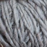 Close-up image of a large bundle of Halcyon Geo Rug Wool by Caledonian Dye Works, showcasing the thick, soft fibers twisted together. The texture is coarse yet fluffy, with subtle variations in the shades of grey and white strands intermingled.