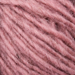 Close-up of a ball of soft, fluffy pink Halcyon Geo Rug Wool by Caledonian Dye Works. The texture showcases fine fibers and a slightly fuzzy appearance, with the strands wound closely together. The yarn has a muted, dusty rose hue.