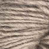 Close-up of a skein of Halcyon Geo Rug Wool by Caledonian Dye Works in a soft, light gray shade with a slightly fuzzy texture. The strands are thick and loosely twisted, creating a cozy look reminiscent of traditional rug wool. The image highlights the intricate details and fibers of the yarn.