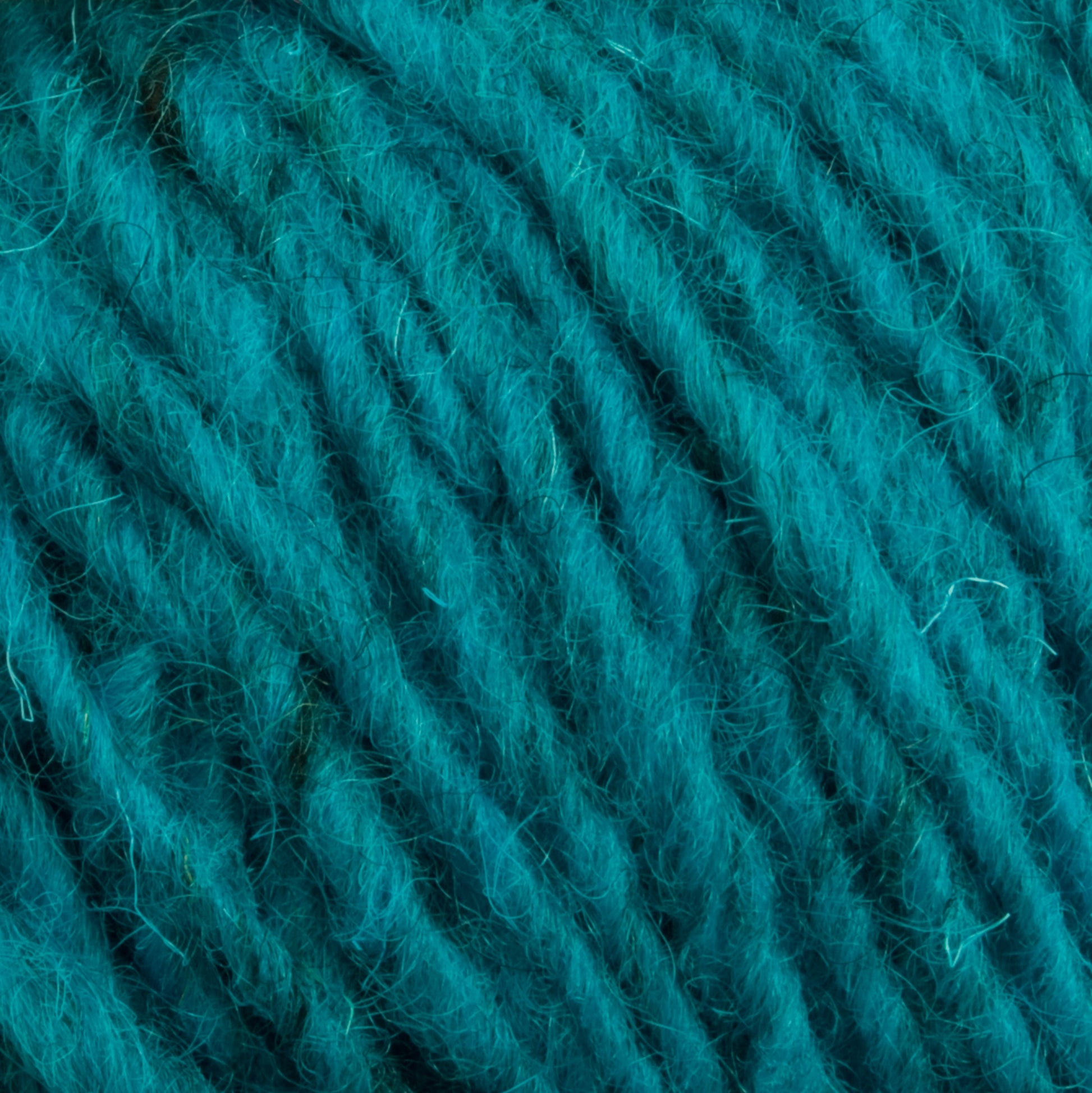 Close-up of thick, teal-colored yarn with a slightly fuzzy texture. The fibers are tightly twisted, creating a soft and rich appearance. The image highlights the detailed texture and vibrant color of the Halcyon Geo Rug Wool by Caledonian Dye Works, showcasing its luxurious feel.