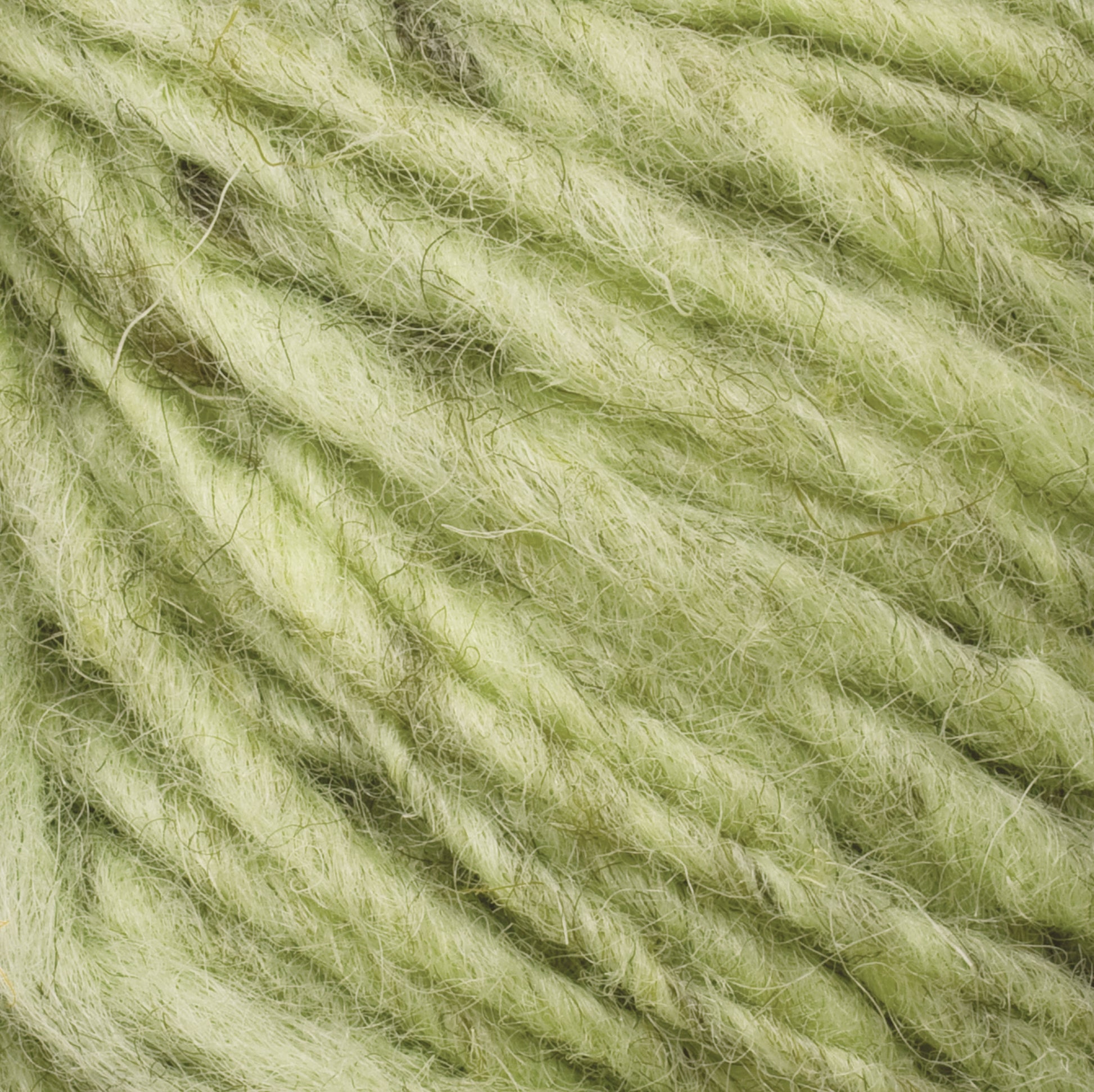 Close-up of soft, green wool yarn fibers, showcasing their tangled and fuzzy texture. The yarn, reminiscent of Halcyon Geo Rug Wool by Caledonian Dye Works, is loosely twisted, creating a thick and bulky appearance with subtle variations in the shades of green.