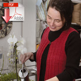 A woman with dark hair, donning a Halcyon Yarn Wildflower Vest in red over a black top, tends to a plant in a cozy room. In the background, shelves adorned with pillows and a decorative mirror can be seen. An Adobe PDF icon with a down arrow is overlaid in the top left corner, indicating that the Wildflower Vest can be downloaded.