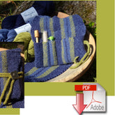 A close-up of a handmade blue and green striped knitted project bag, known as the Felted Accessory Clutch from Halcyon Yarn, filled with knitting needles and tools. The bag, crafted from worsted weight wool yarn, is displayed outdoors on a wooden bowl with yarn skeins in the background. An Adobe PDF download icon is placed on the lower right corner.