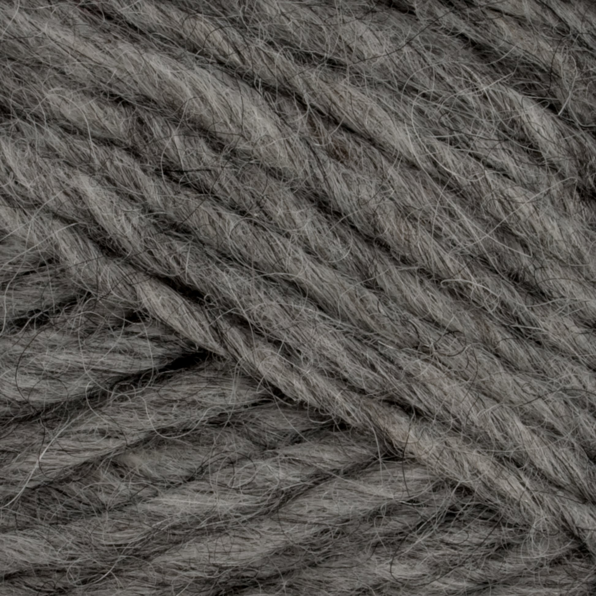 Close-up view of a ball of grey Lopi Alafoss Icelandic Wool Yarn by Berroco, Inc. The yarn fibers appear soft and thick, with a slightly fuzzy texture perfect for Icelandic pullovers. The strands are twisted together, showing varied light and dark grey tones.