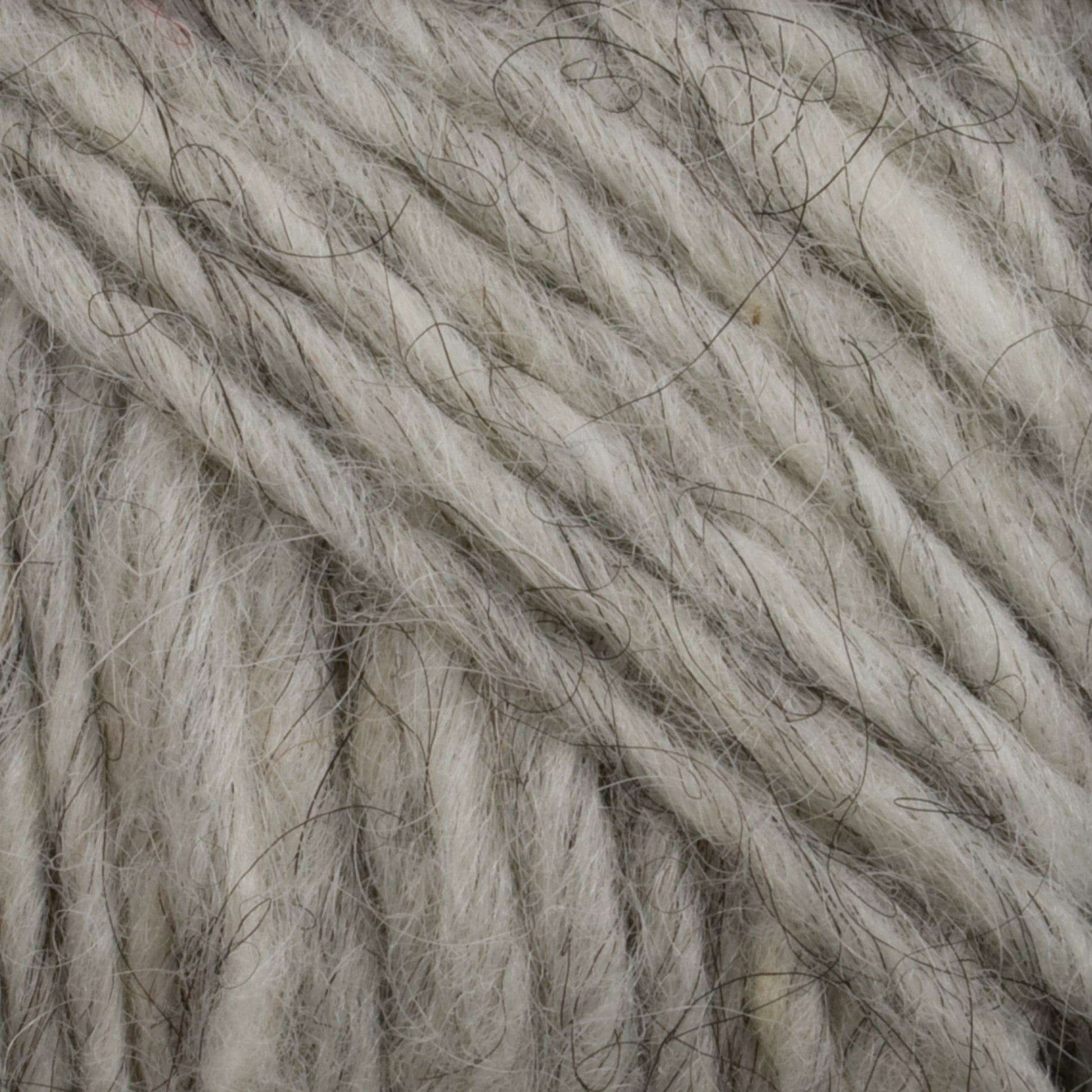 Close-up image showing a bundle of thick, gray Lopi Alafoss Icelandic Wool Yarn by Berroco, Inc. with a textured, fibrous appearance. The strands intertwine, showcasing the natural variances in shade and the presence of darker threads intertwined with the lighter wool. This exquisite material is perfect for Icelandic pullovers.