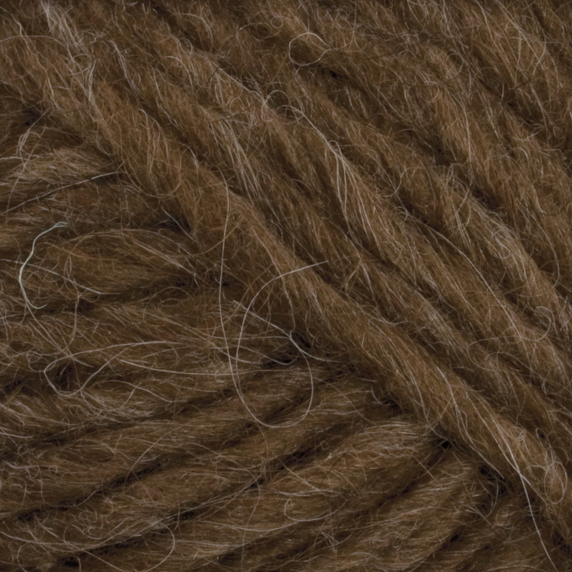 Close-up image of thick, brown Lopi Alafoss Icelandic Wool Yarn by Berroco, Inc. The strands are tightly wound together with some loose fibers visible on the surface, giving it a slightly fuzzy texture perfect for crafting Icelandic pullovers or felted mittens.