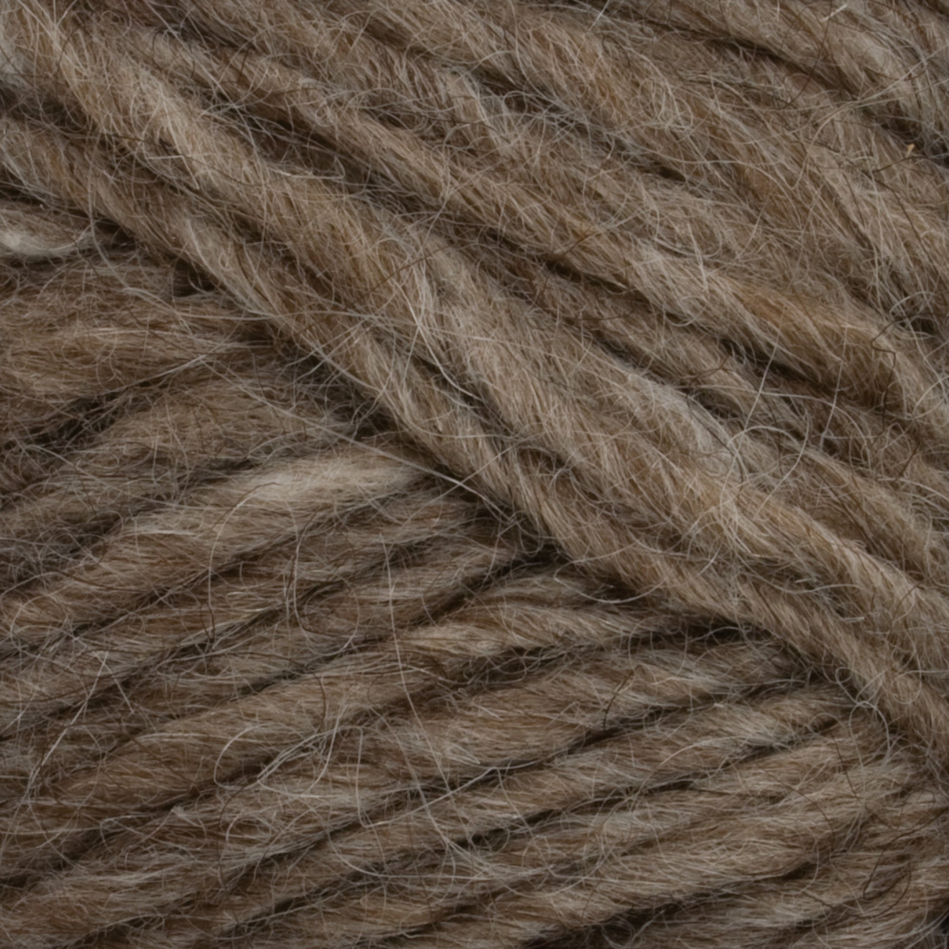 Close-up image of brown yarn fibers tightly intertwined. The yarn, reminiscent of Icelandic pullovers, has a speckled appearance with subtle variations in shades of brown and hints of gray, giving it a natural and textured look. The fibers appear soft and slightly fuzzy, akin to Lopi Alafoss Icelandic Wool Yarn by Berroco, Inc.