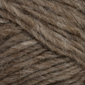 Close-up image of brown yarn fibers tightly intertwined. The yarn, reminiscent of Icelandic pullovers, has a speckled appearance with subtle variations in shades of brown and hints of gray, giving it a natural and textured look. The fibers appear soft and slightly fuzzy, akin to Lopi Alafoss Icelandic Wool Yarn by Berroco, Inc.