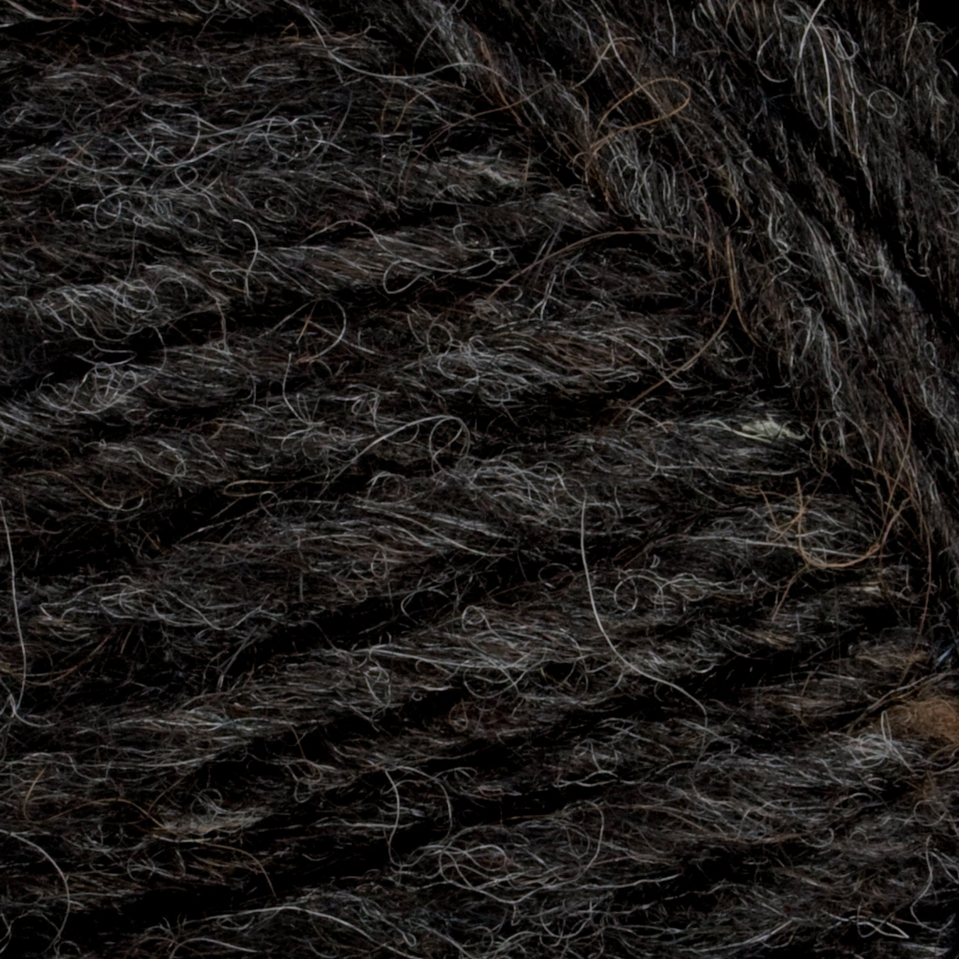 Close-up of dark grey and black Lopi Alafoss Icelandic Wool Yarn from Berroco, Inc., highlighting the texture and intertwined strands. The yarn showcases a slightly rough and fibrous texture with a mix of varying shades of grey and black, making it ideal for crafting rugged felted mittens or traditional Icelandic pullovers.