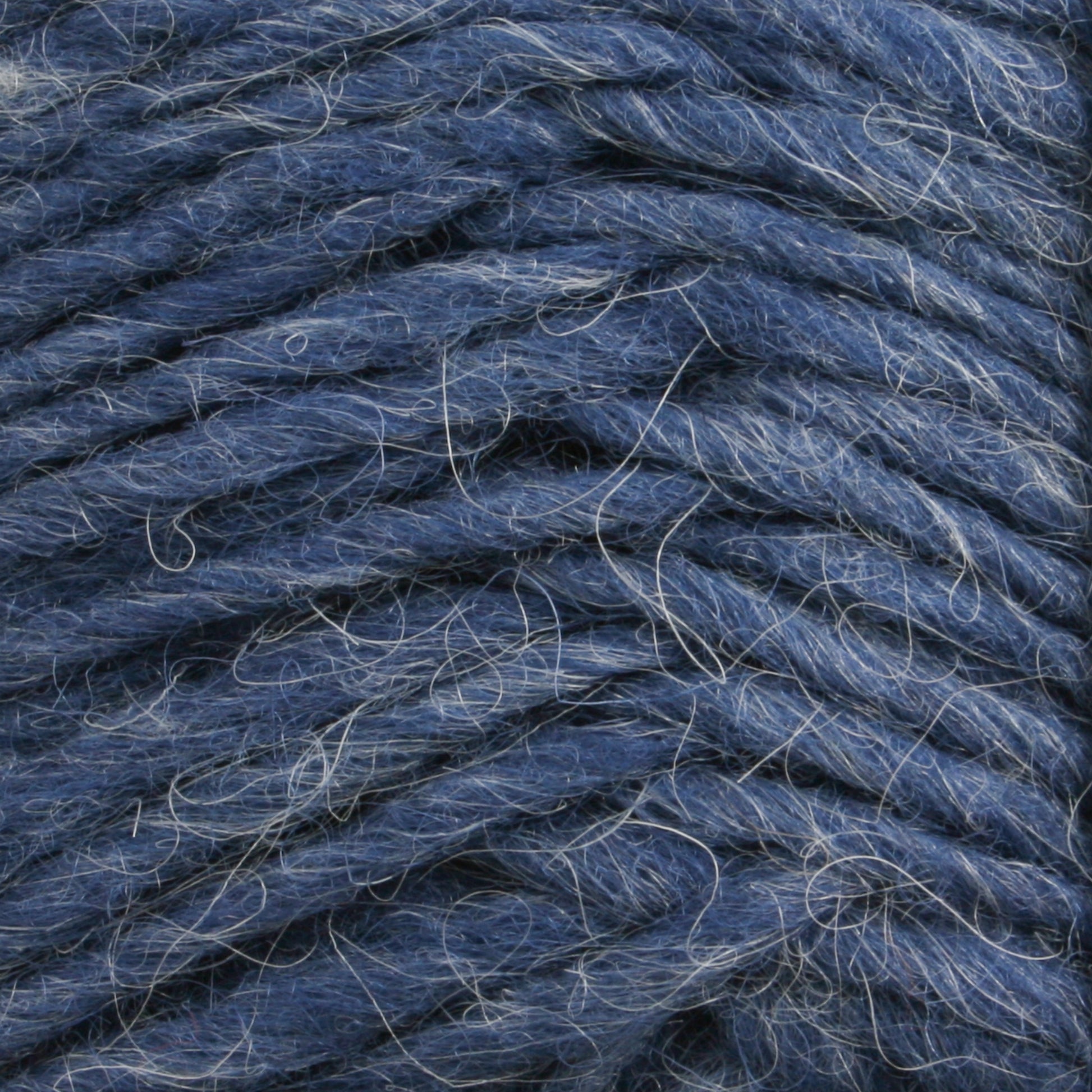 Close-up of a thick, blue Lopi Alafoss Icelandic Wool Yarn from Berroco, Inc., featuring a slightly rough texture. The intertwined fibers with some loose strands visible give it a slightly fuzzy appearance, reminiscent of the kind used in traditional Icelandic pullovers.