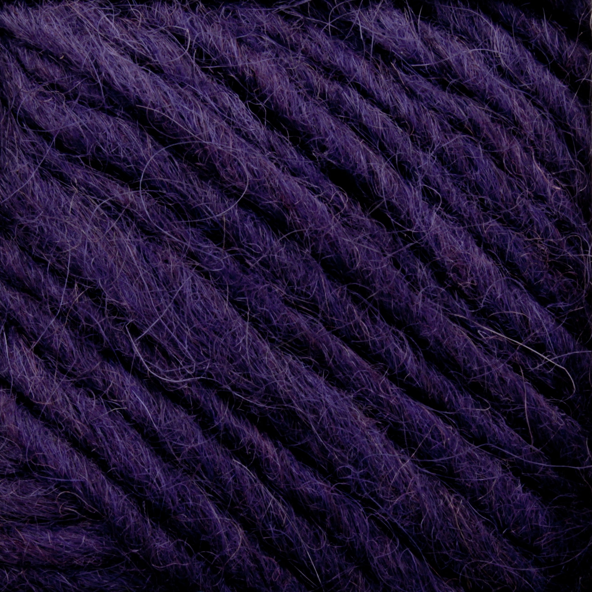 Close-up image of Lopi Alafoss Icelandic Wool Yarn by Berroco, Inc., showcasing its deep purple hue, textured and twisted strands. The yarn appears thick, with individual fibers visible for a slightly fuzzy appearance. The overall texture looks soft and plush, reminiscent of the high-quality yarn used in crafting cozy Icelandic pullovers.