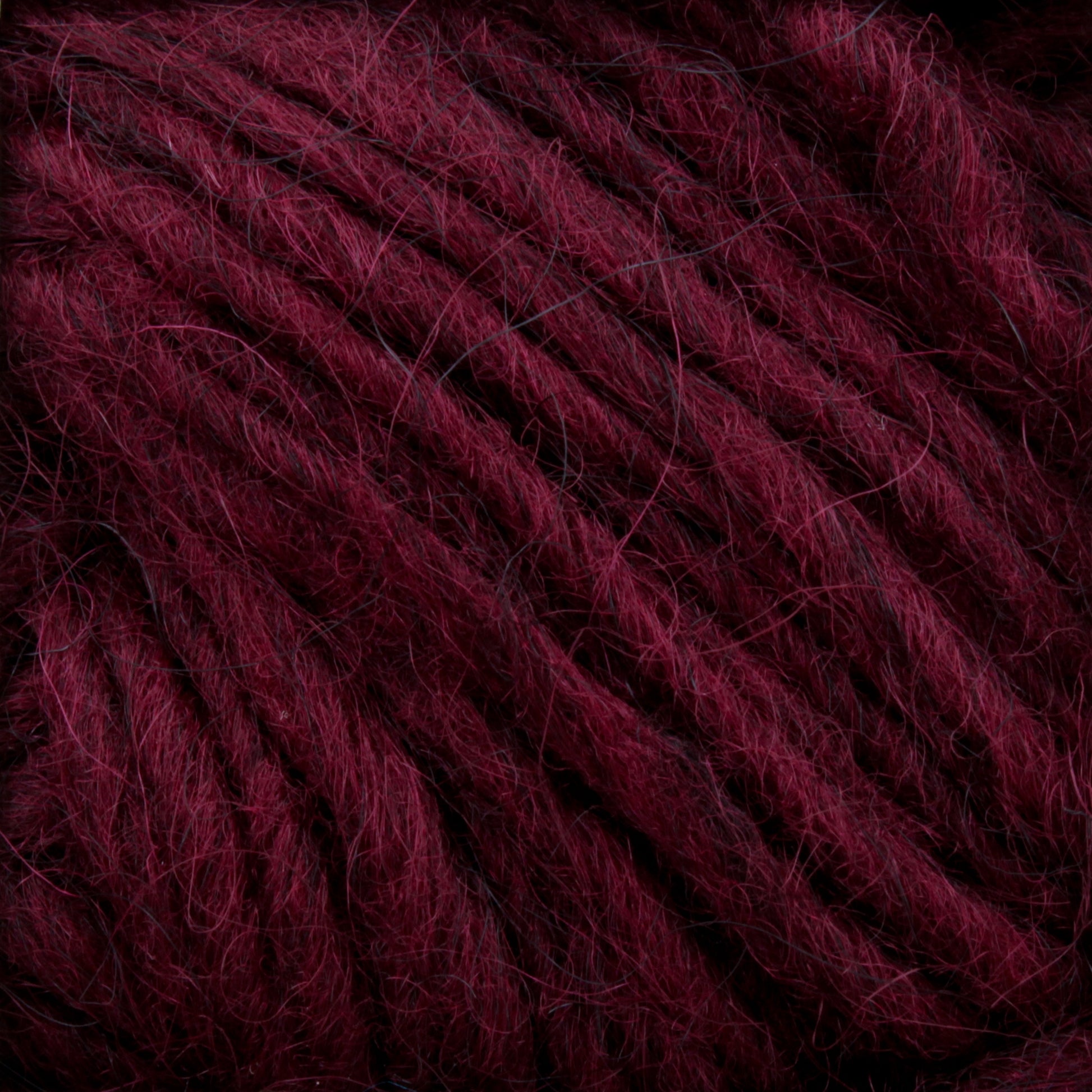 Close-up of Lopi Alafoss Icelandic Wool Yarn by Berroco, Inc., showcasing its deep burgundy hue and thick, fuzzy texture with intricately intertwined fibers. The rich color and soft appearance suggest it would be cozy for knitting or crocheting projects, making it perfect for crafting felted mittens or classic Icelandic pullovers.