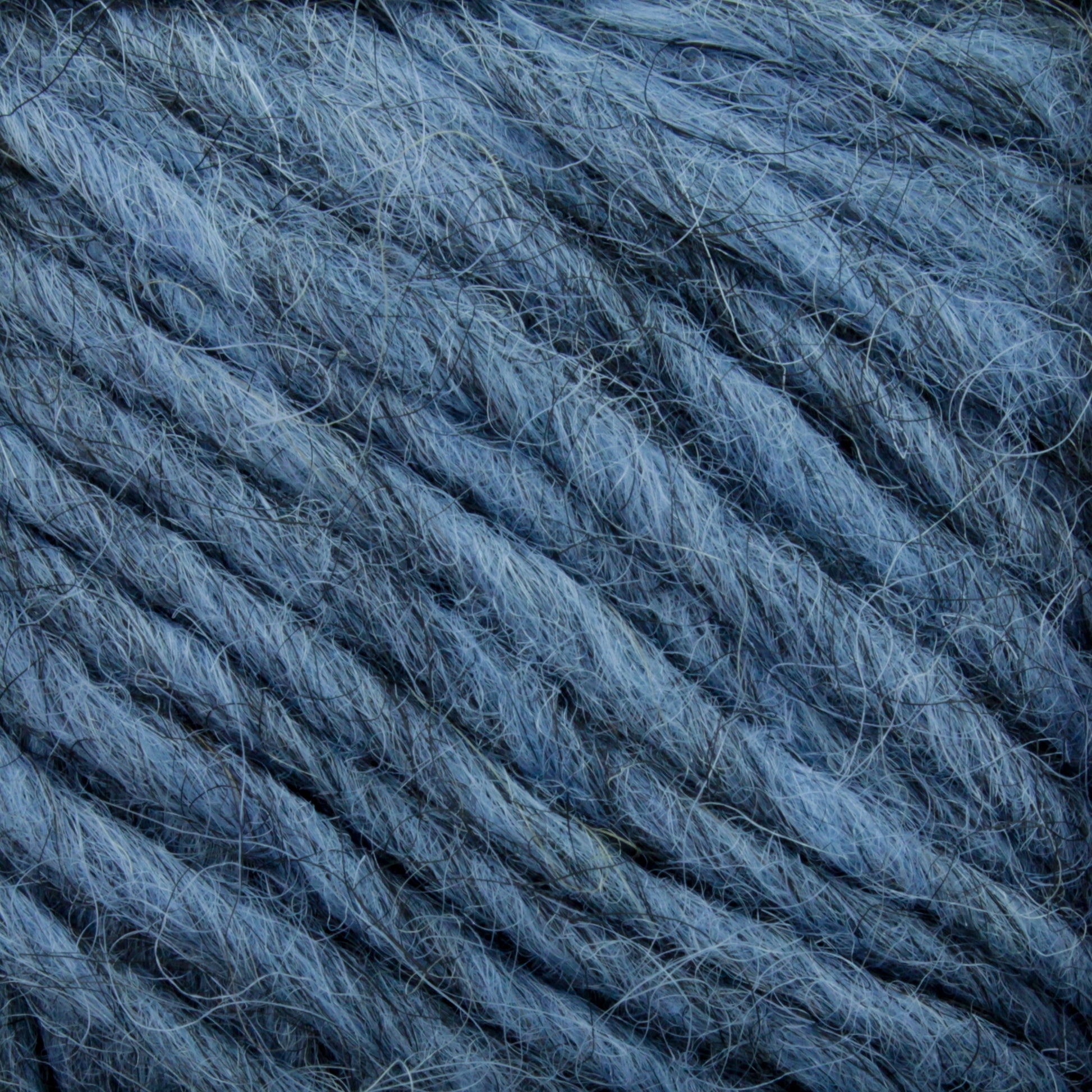 Close-up of blue-gray yarn fibers intertwined, reminiscent of Lopi Alafoss Icelandic Wool Yarn by Berroco, Inc. The texture is soft and slightly fuzzy, showcasing individual threads and strands woven together in a loose, thick pattern.