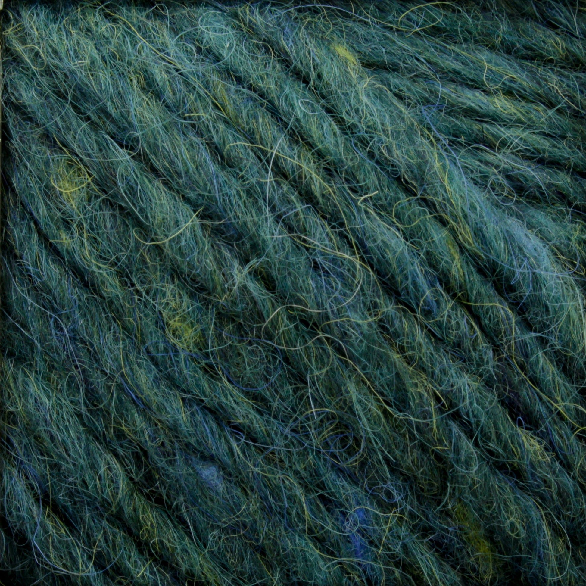 Close-up image of the Berroco, Inc. Lopi Alafoss Icelandic Wool Yarn in green and blue variegated hues, featuring a soft, fuzzy texture. The twisted yarn strands create a thick and cozy appearance reminiscent of traditional Icelandic pullovers. The blend of colors provides a natural, earthy feel.