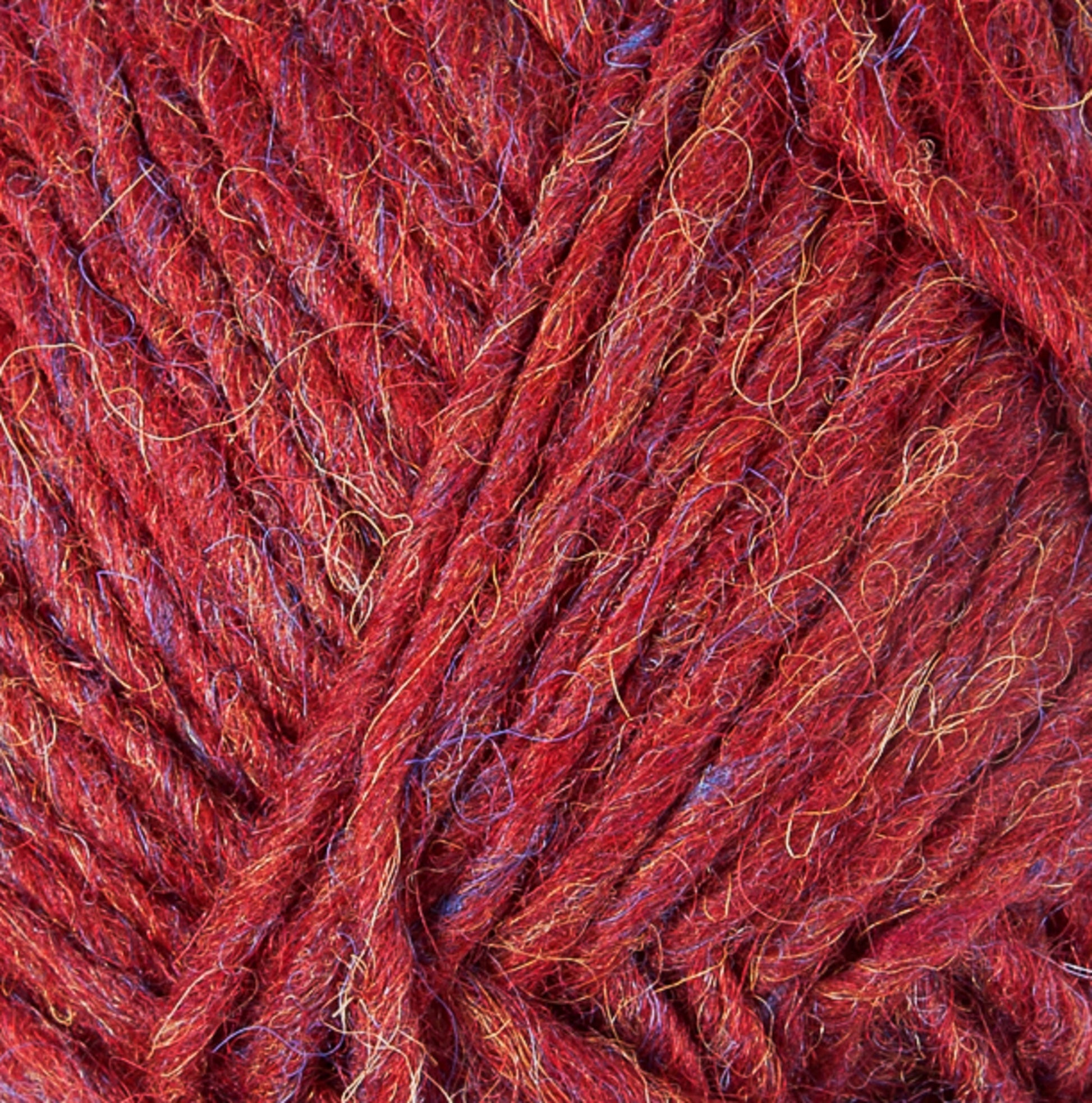 Close-up image of Lopi Alafoss Icelandic Wool Yarn by Berroco, Inc. in red with subtle interwoven blue and gold fibers creating a textured appearance. The thick, slightly fuzzy strands are reminiscent of the yarn used in Icelandic pullovers, with loose ends visible in some areas. The yarn appears to be bundled together in a tidy manner.