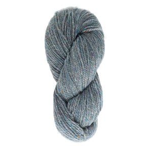 A neatly twisted hank of light blue Harrisville Designs' Peace Fleece Yarn, speckled with small flecks of other colors like brown and purple. This worsted weight knitting yarn is a gentle wool and mohair blend, appearing soft and thick—making it perfect for knitting or crocheting projects.