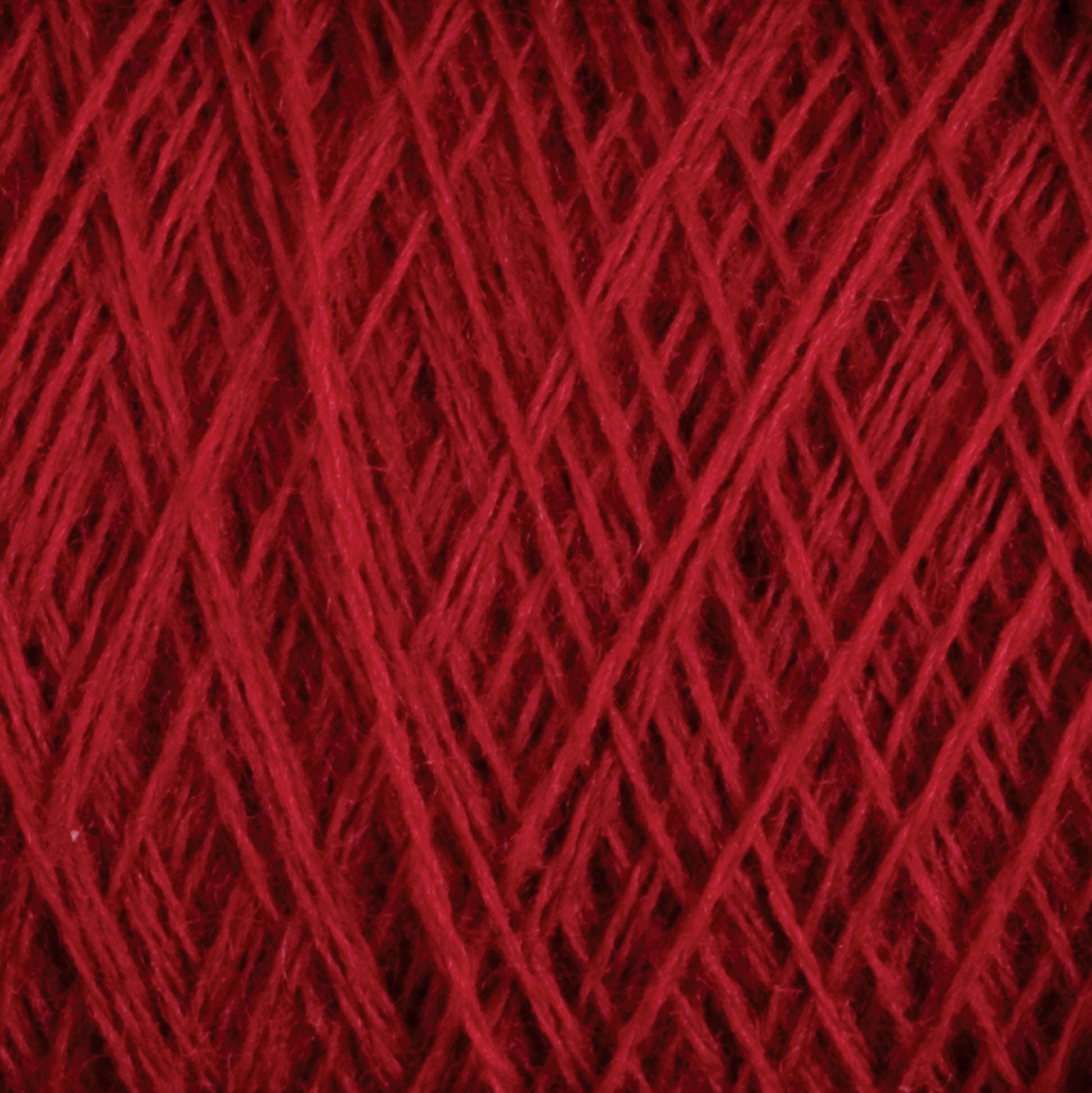 Close-up view of a ball of JaggerSpun Maine Line 2/8 Yarn | Mini-cone by Jagger Brothers, Inc., showcasing the intricate interwoven strands and the soft, fuzzy texture typical of worsted spun yarn. The crisscross pattern highlights the thickness and richness of the red color, reminiscent of fine knitting or weaving.