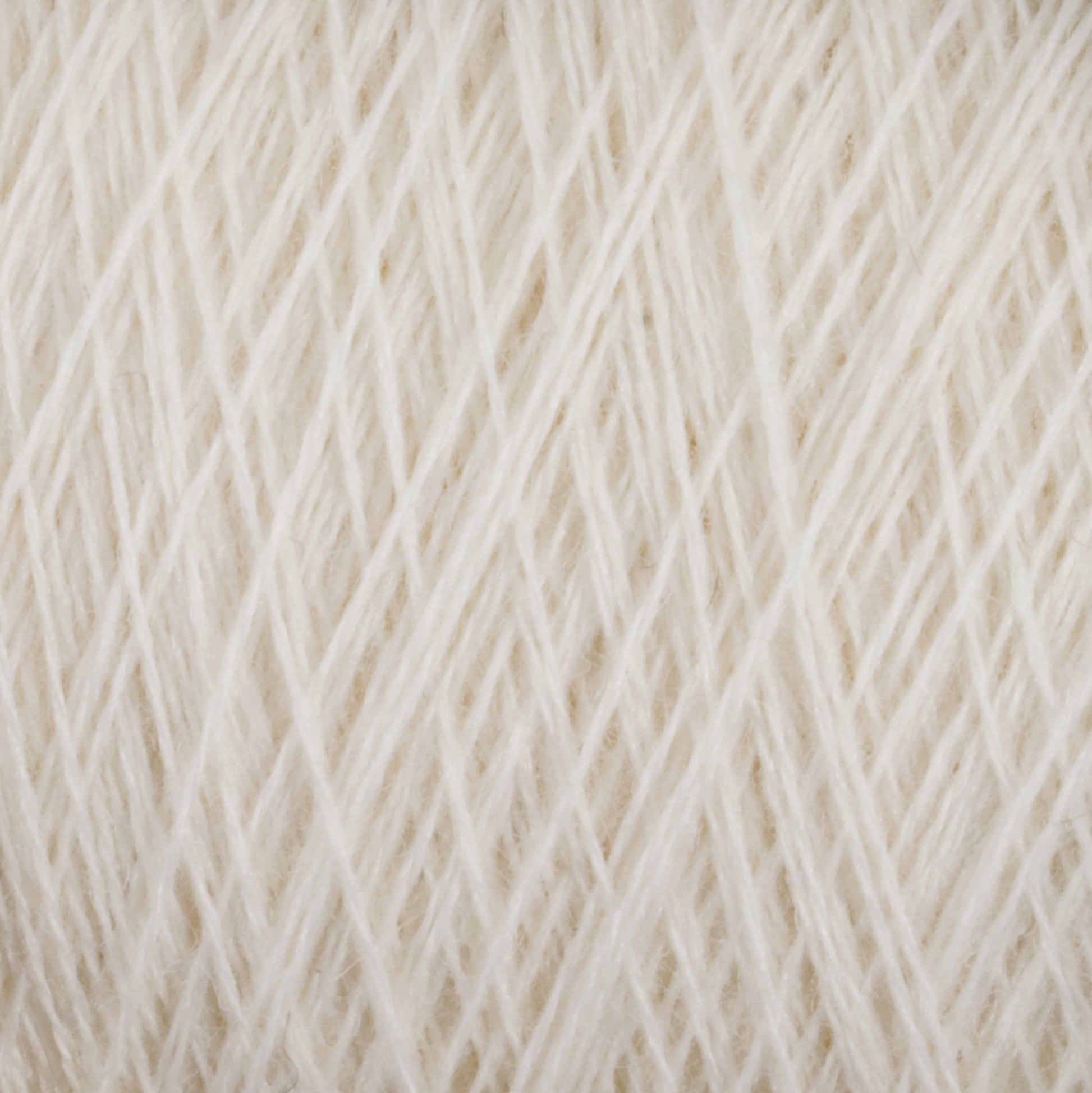 Close-up image of a soft, cream-colored JaggerSpun Maine Line 2/8 Yarn | Mini-cone by Jagger Brothers, Inc. The yarn is tightly wound and reveals intricate patterns of interwoven fibers. The texture appears delicate and fluffy, hinting at a cozy and warm fabric when knitting or crocheting with this worsted spun yarn.