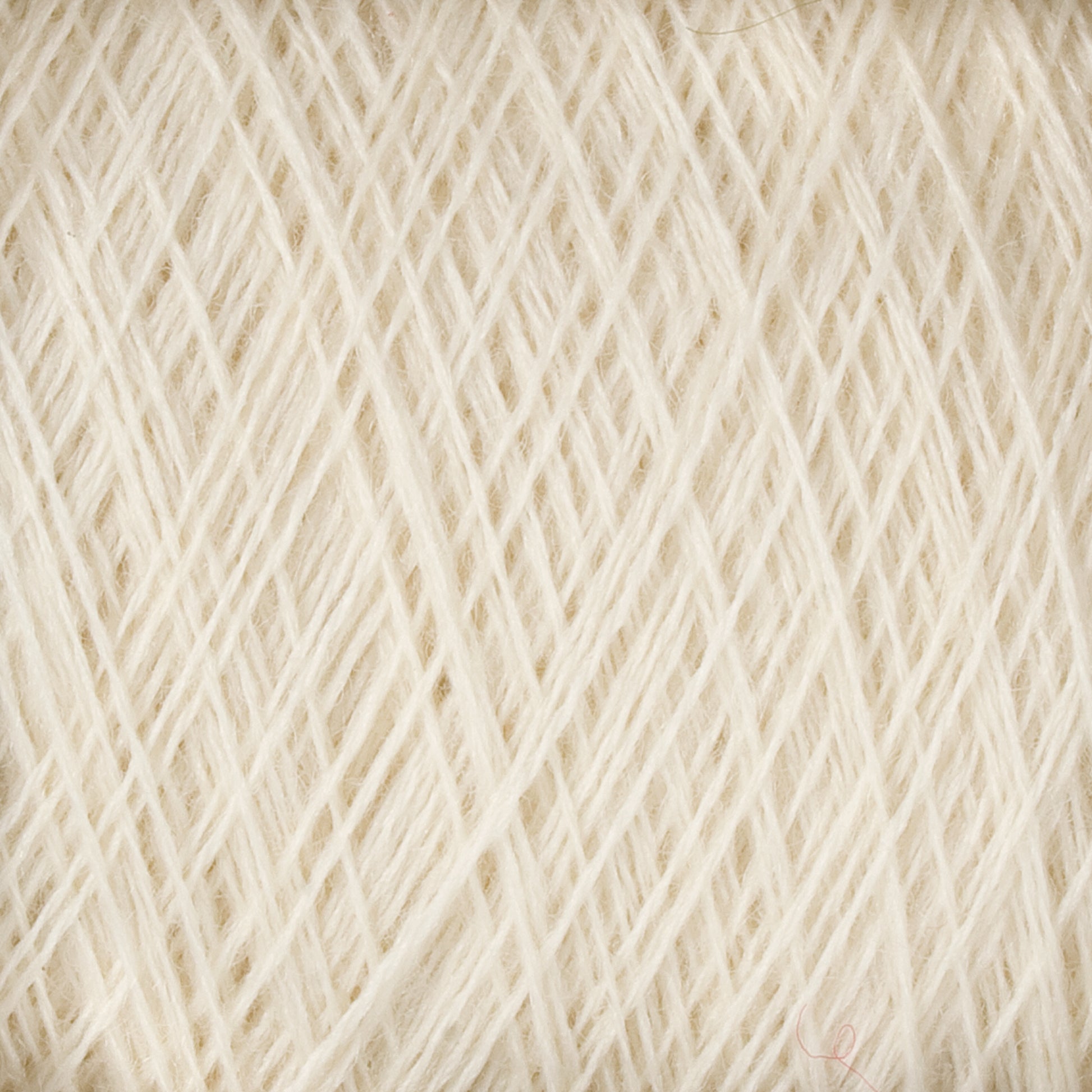 A close-up image of JaggerSpun Maine Line 2/8 Yarn | Mini-cone by Jagger Brothers, Inc. reveals intricate patterns of tightly interwoven light cream-colored fibers. The soft and slightly fuzzy texture suggests this worsted spun yarn is ideal for knitting or weaving delicate textiles.