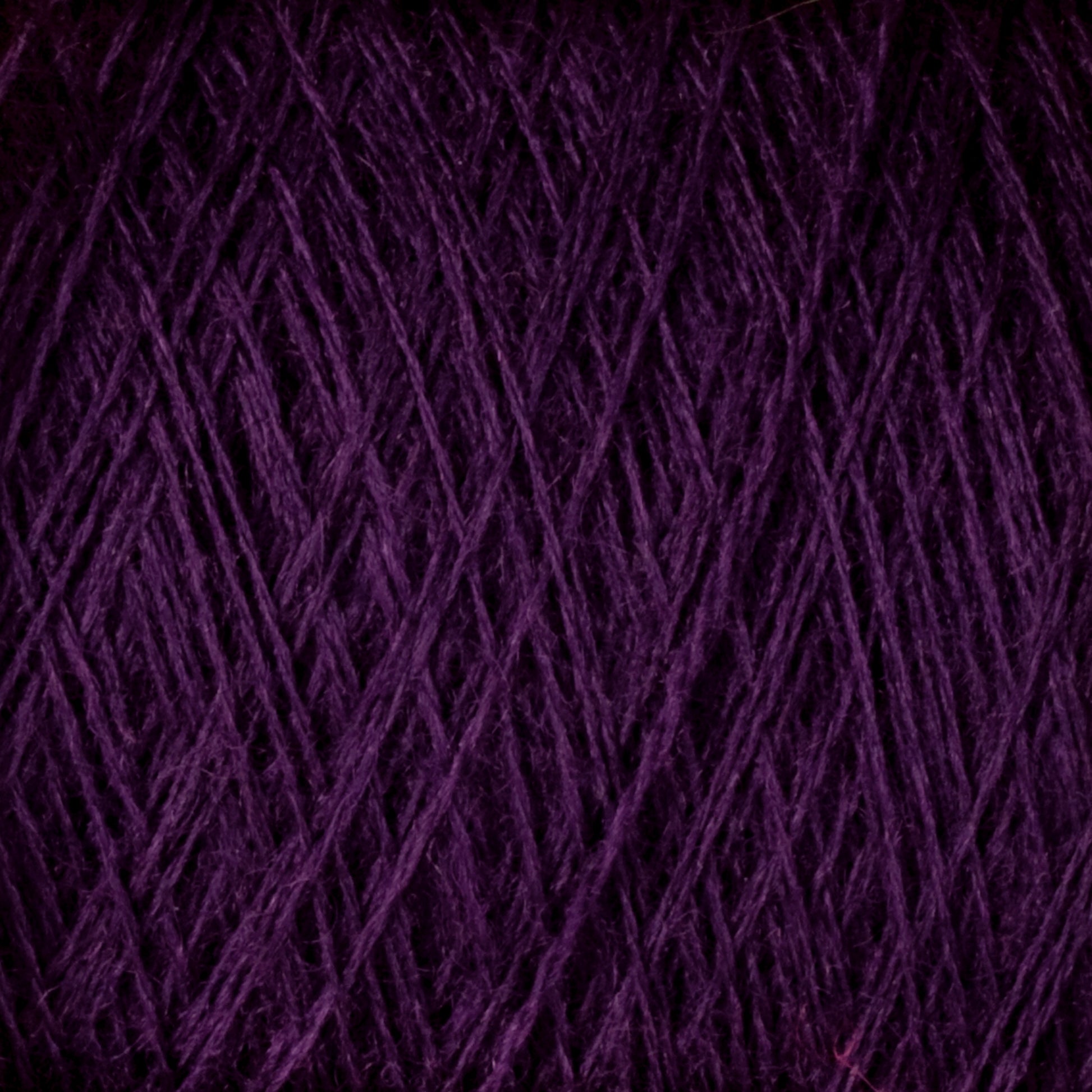 Close-up image of JaggerSpun Maine Line 2/8 Yarn Mini-cone by Jagger Brothers, Inc., showcasing a ball of dark purple, worsted spun yarn. The fibers are tightly wound, with visible strands crisscrossing each other, creating a textured and intricate pattern perfect for knitting or weaving projects.