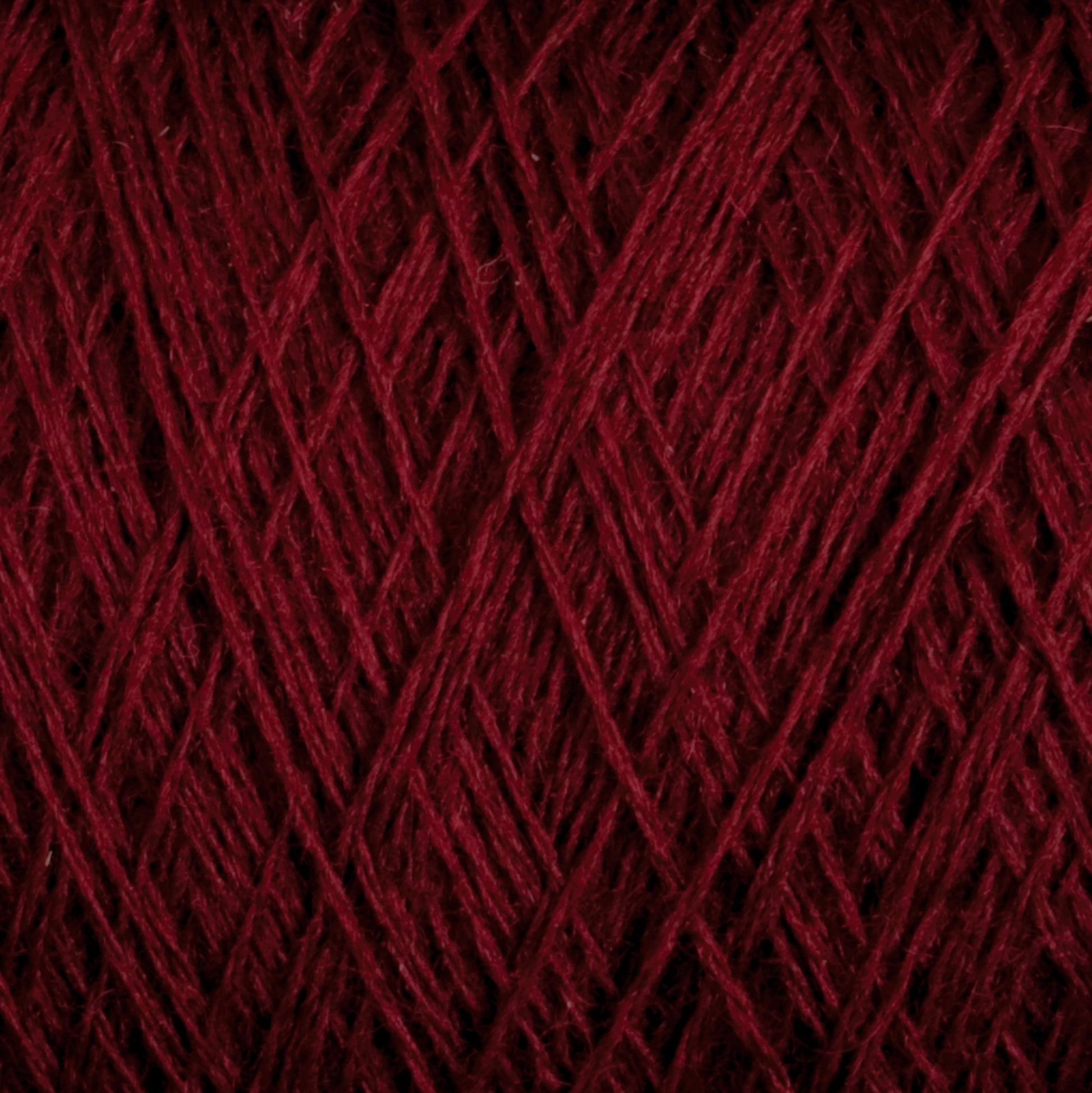 Close-up shot of JaggerSpun Maine Line 2/8 Yarn | Mini-cone from Jagger Brothers, Inc., wound into a dense, intricate ball. The texture is clearly visible, showcasing its fibrous nature and overlapping strands, perfect for weaving or knitting. The deep red color is rich and consistent throughout.