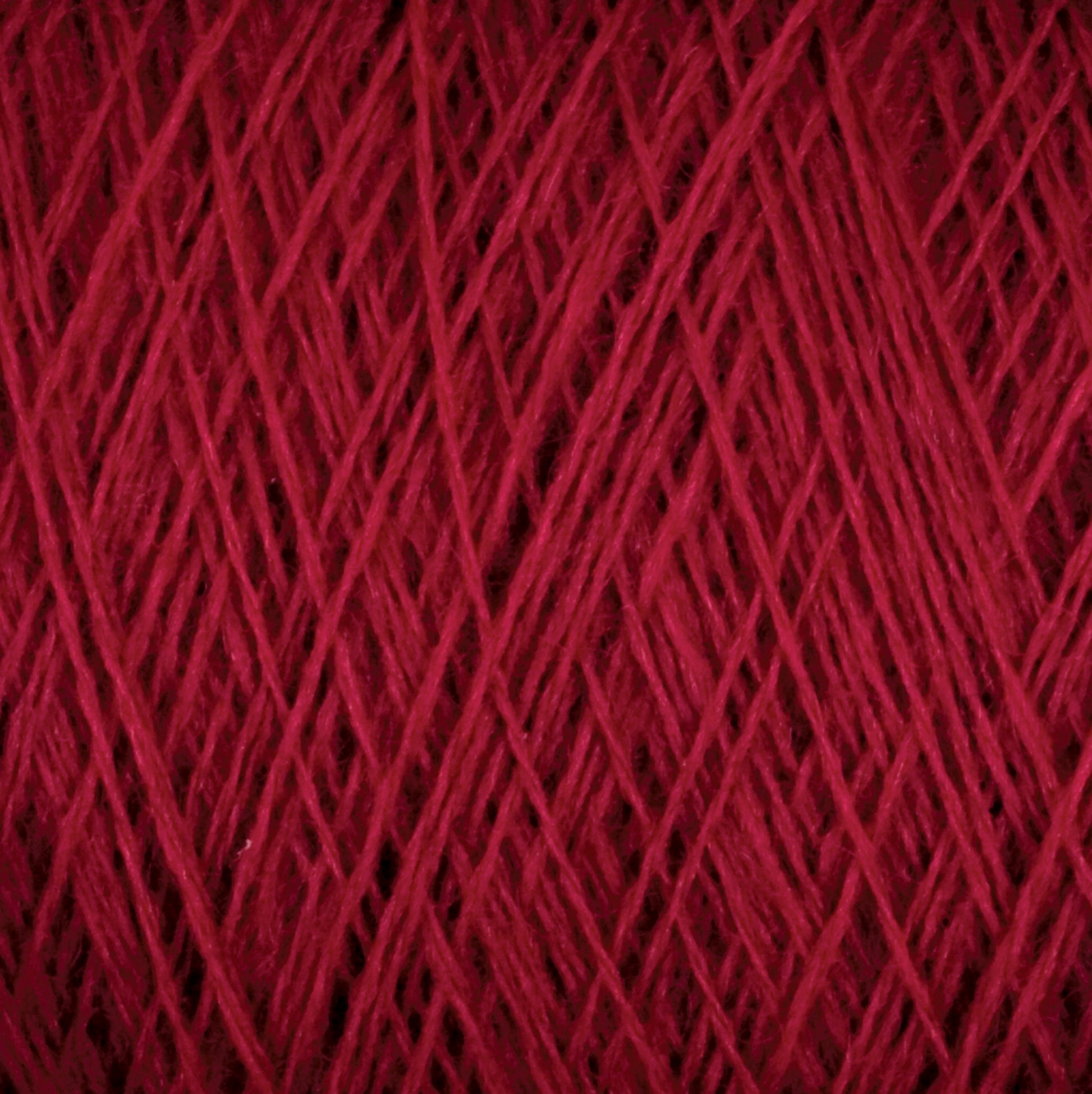 Close-up of Jagger Brothers, Inc.'s JaggerSpun Maine Line 2/8 Yarn | Large Cone in red 27.5 micron worsted spun wool wound into a ball. The tightly wrapped fibers form diagonal lines, creating a textured and intricate pattern with varying shades of red, perfect for both commercial and recreational knitters.