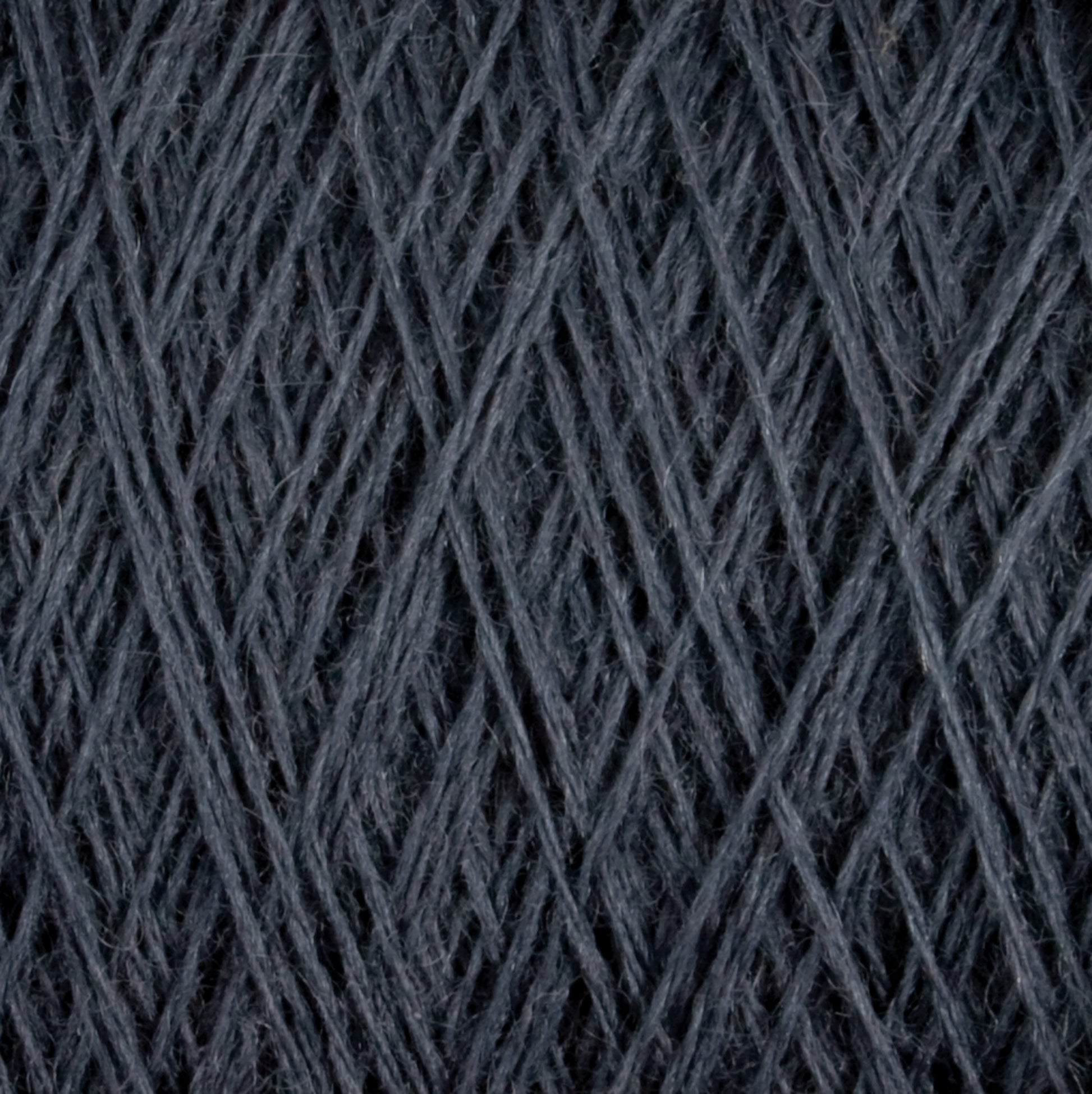 Close-up of dark grey JaggerSpun Maine Line 2/8 Yarn | Large Cone from Jagger Brothers, Inc., showing the intricately wound worsted spun wool with visible fibers. The 27.5-micron strands are tightly interwoven, forming a textured and detailed pattern. The photo highlights the texture and complexity appreciated by both commercial and recreational knitters.