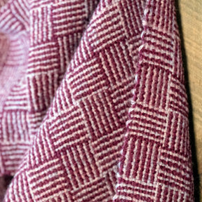 Close-up of Halcyon Yarn's Rivers and Roads Woven Scarf, download, showcasing its folded fabric with a textured, geometric pattern in shades of purple. The design resembles a wool scarf pattern, featuring small alternating square segments arranged in a grid layout to create a visually intricate and tactile effect.