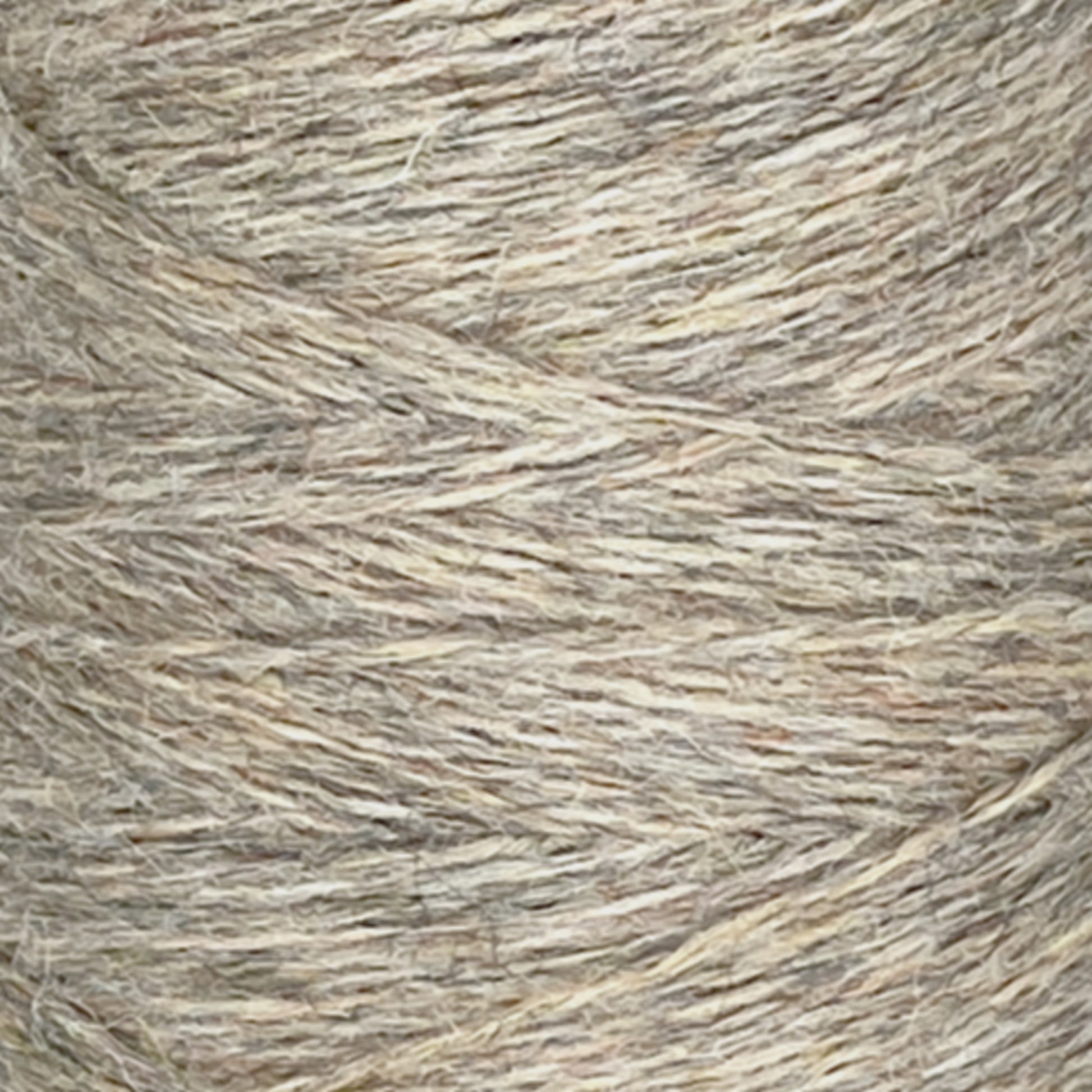 Close-up image of a spool of JaggerSpun Heather 2/8 | Large Cone yarn by Jagger Brothers, Inc., featuring various shades of tan and light brown fibers. The yarn's texture appears slightly coarse and is tightly wound around the spool, showcasing the interwoven strands typical of worsted spun quality.