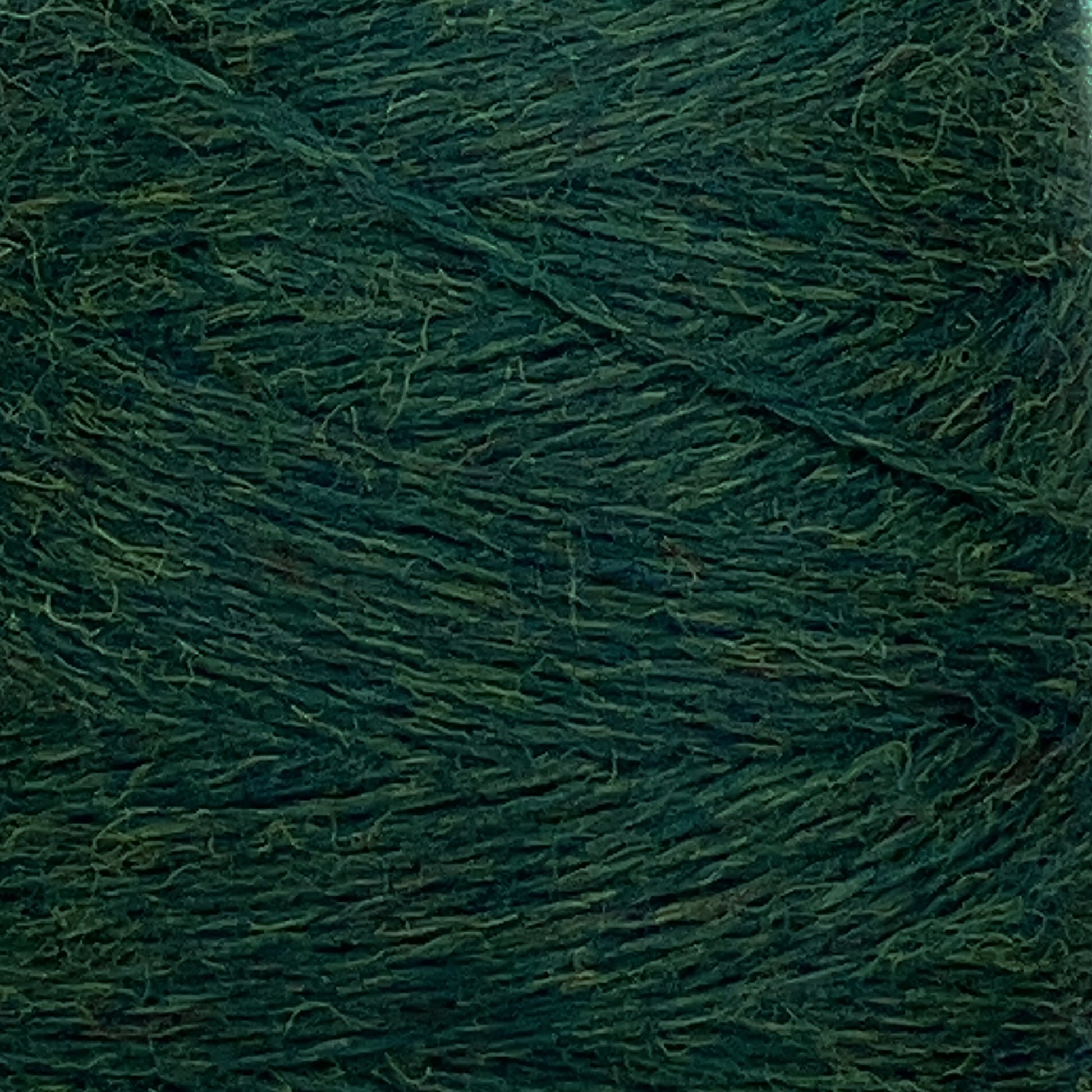 A close-up view of a spool of dark green yarn. The JaggerSpun Heather 2/8 Mini-cone from Jagger Brothers, Inc. is tightly wound, showcasing its texture and slight fuzziness. The image highlights the various shades of green within the wool, dyed using low-impact synthetic dyes for an eco-friendly touch.