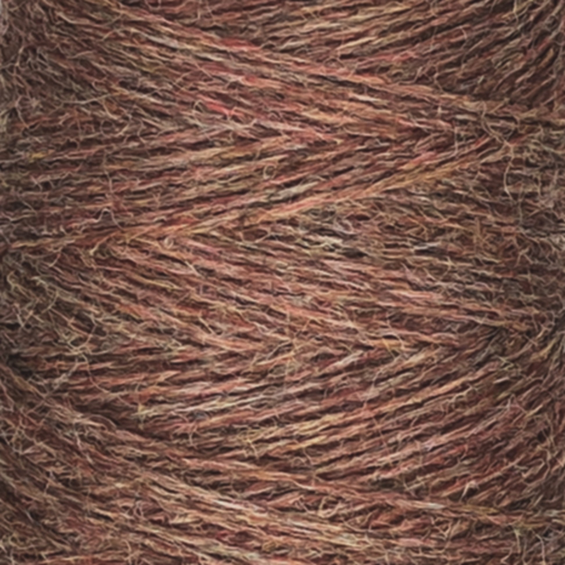 A close-up image of a spool of JaggerSpun Heather 2/8 Mini-cone yarns by Jagger Brothers, Inc. The yarn displays a mix of earthy tones, primarily browns and reds, with varying textures and thicknesses visible. The fibers appear to be tightly wound together using low-impact synthetic dyes.