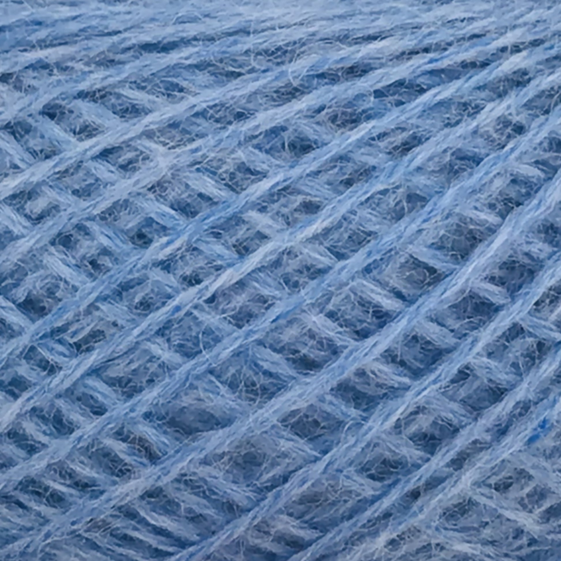 Close-up image of JaggerSpun Heather 2/8 in a light blue shade, showcasing its soft, fluffy texture and intricate, crisscrossing fibers. The detailed pattern and gentle hues emphasize the thread’s delicacy and suitability for knitting or crocheting projects, embodying the refined quality of Jagger Brothers, Inc.'s yarns.