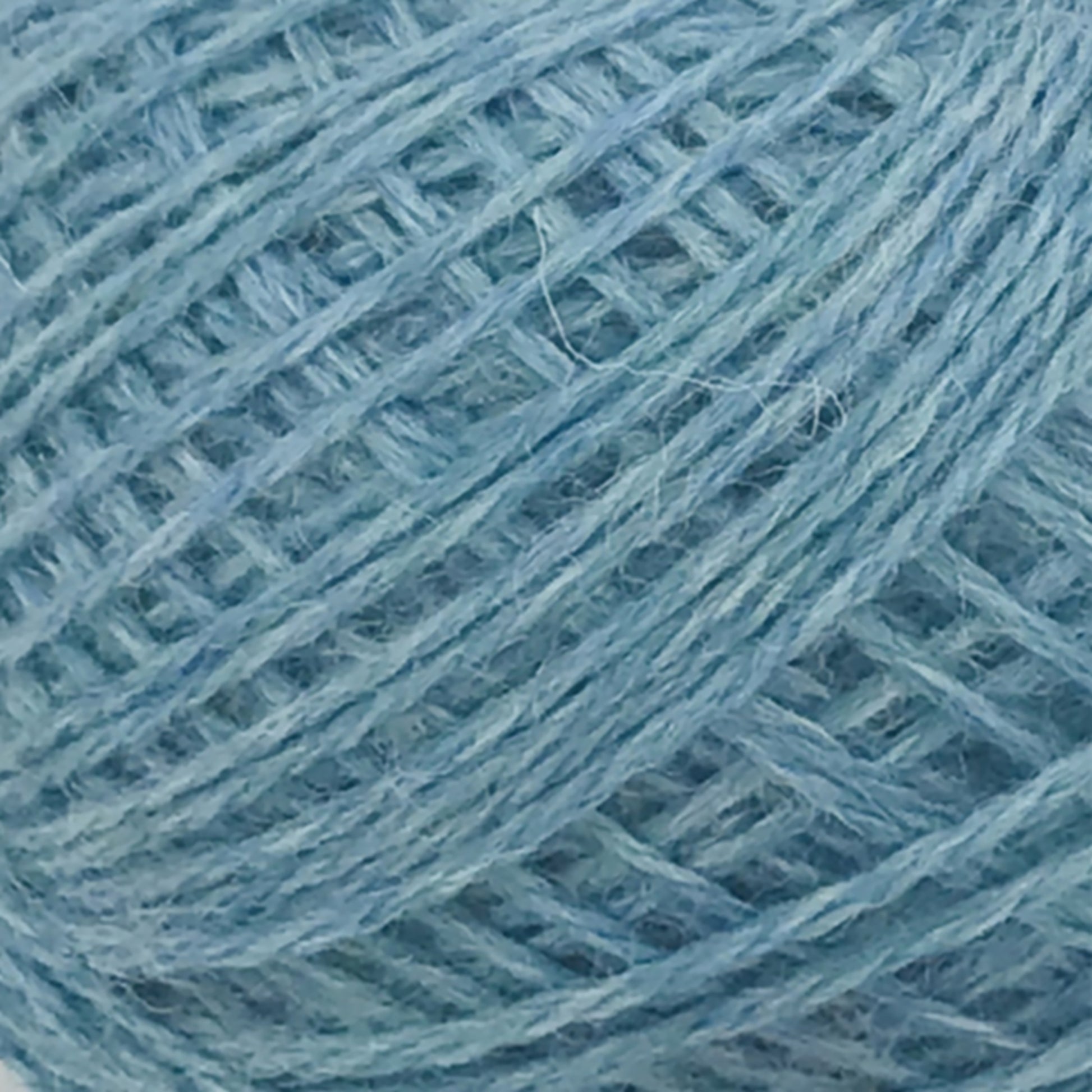 A close-up image of JaggerSpun Heather 2/8 yarns from Jagger Brothers, Inc., intricately wound into a mini-cone. The strands of yarn are clearly visible, showcasing the fibrous texture and slight variations in the blue color, ranging from pale blue to a slightly darker shade.