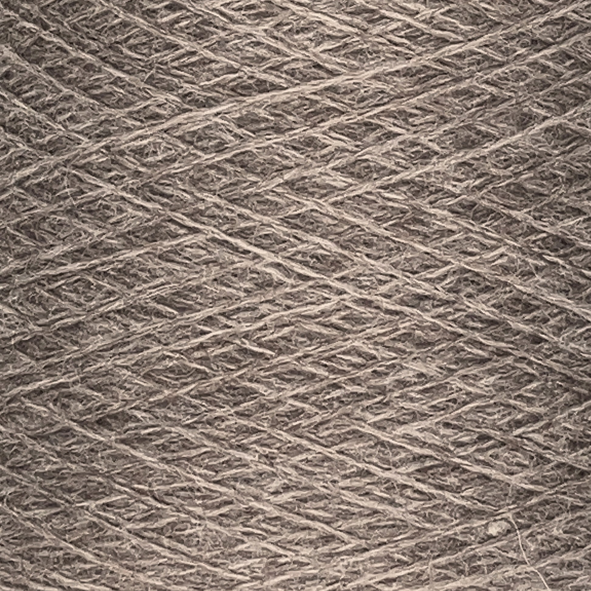 Close-up image of a ball of JaggerSpun Heather 2/8 | Mini-cone yarn from Jagger Brothers, Inc., with visible strands tightly wound together. The texture and individual fibers are clearly visible, showcasing the material. The yarn, dyed with low-impact synthetic dyes, features a neutral, natural tone.