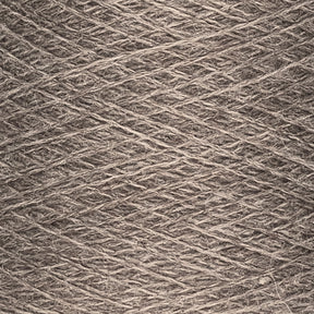 Close-up of a spool of JaggerSpun Heather 2/8 yarn by Jagger Brothers, Inc., showcasing the light brown strands intricately wound together into a dense, continuous pattern. The fibers appear evenly spun, creating a uniform, crisscrossed surface typical of worsted spun techniques.