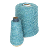 Two spools of blue wool yarns are placed side by side on a plain white background. The JaggerSpun Heather 2/8 large cone, produced by Jagger Brothers, Inc., is cylindrical and stands behind the smaller cone-shaped spool, showcasing the quality of worsted spun fibers.