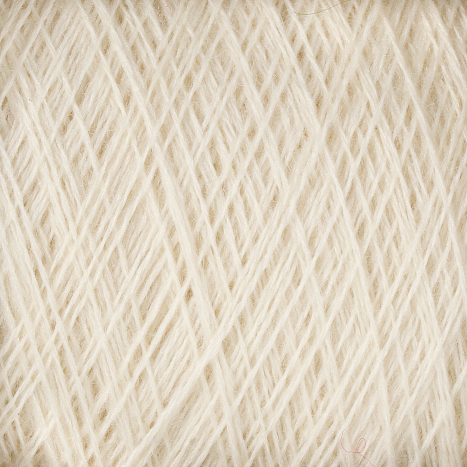 A close-up image of JaggerSpun Superfine Merino 2/18 Yarn Mini-cone by Jagger Brothers, Inc., wound into a tight, dense ball, showcasing the intricate crisscross patterns of the fine cream-colored threads.