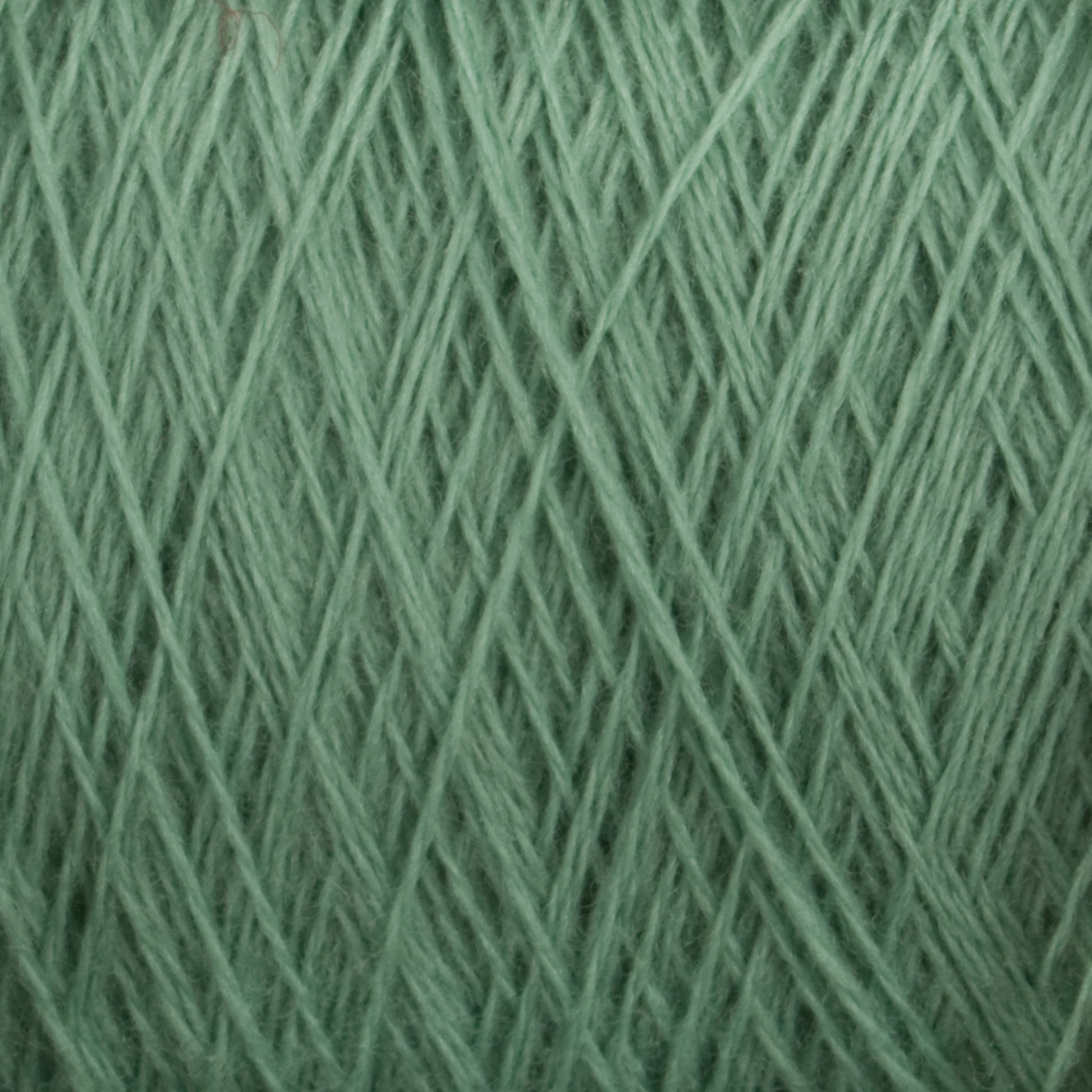 Close-up image of a spool of Jagger Brothers, Inc.'s JaggerSpun Superfine Merino 2/18 Yarn on a large cone, showcasing the detailed intertwining fibers. The texture is soft with a light pastel green hue. This worsted weight merino wool features a crisscross pattern, highlighting both its delicate and sturdy composition—a dream for hand knitters.