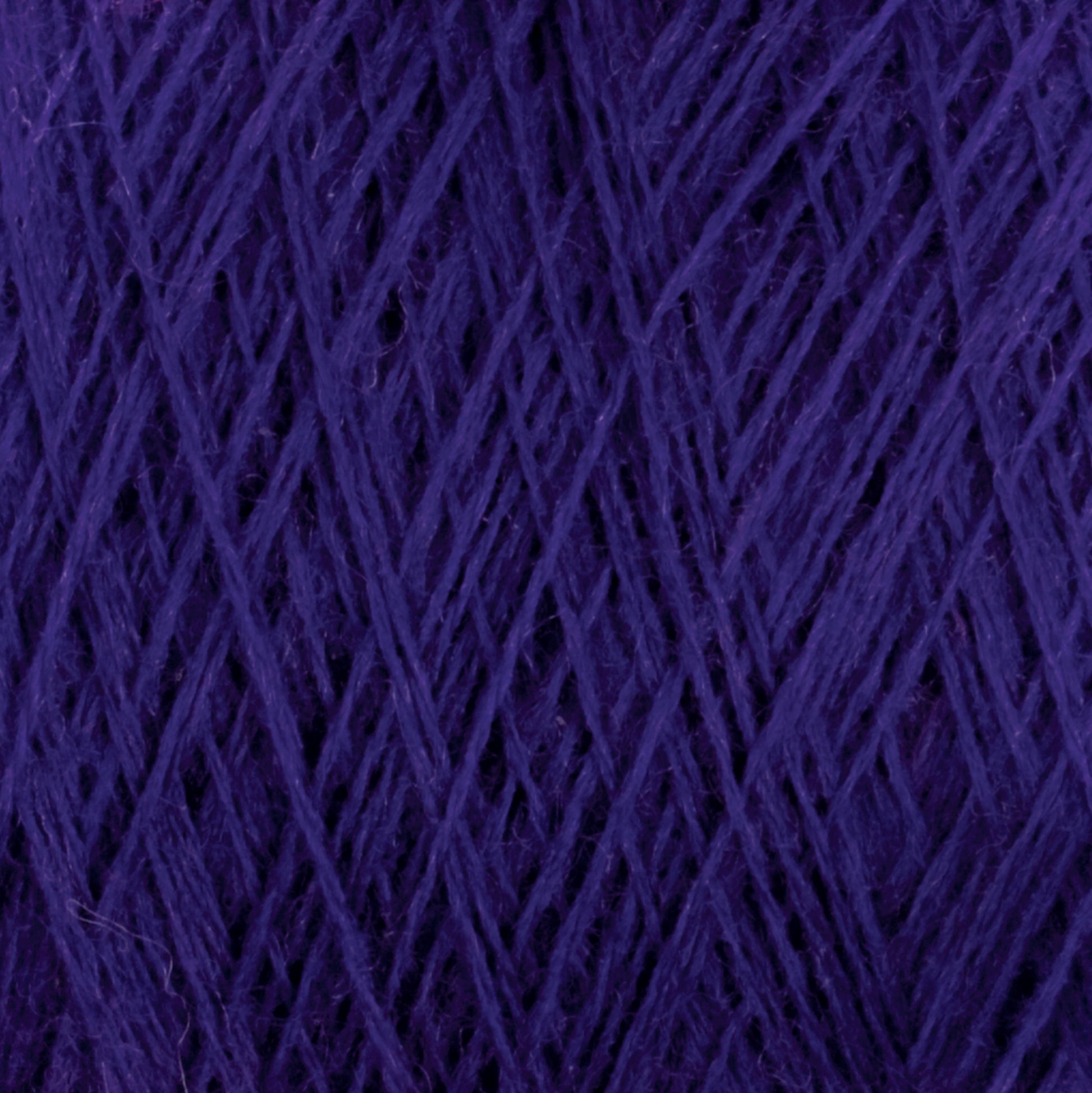 Close-up of JaggerSpun Superfine Merino 2/18 Yarn from Jagger Brothers, Inc., showcasing its deep purple color and intricate texture. Made from luxurious merino wool, the worsted weight strands are tightly wound into a large cone, creating a dense and detailed pattern that highlights the yarn's smooth yet slightly fuzzy surface—ideal for hand knitters.