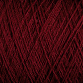 Close-up view of a tightly wound ball of deep red JaggerSpun Superfine Merino 2/18 Yarn from Jagger Brothers, Inc. The threads are intricately interwoven, creating a textured pattern with varying shades of red due to the light and shadow. The image emphasizes the fibrous and detailed nature of this hand knitters yarn.