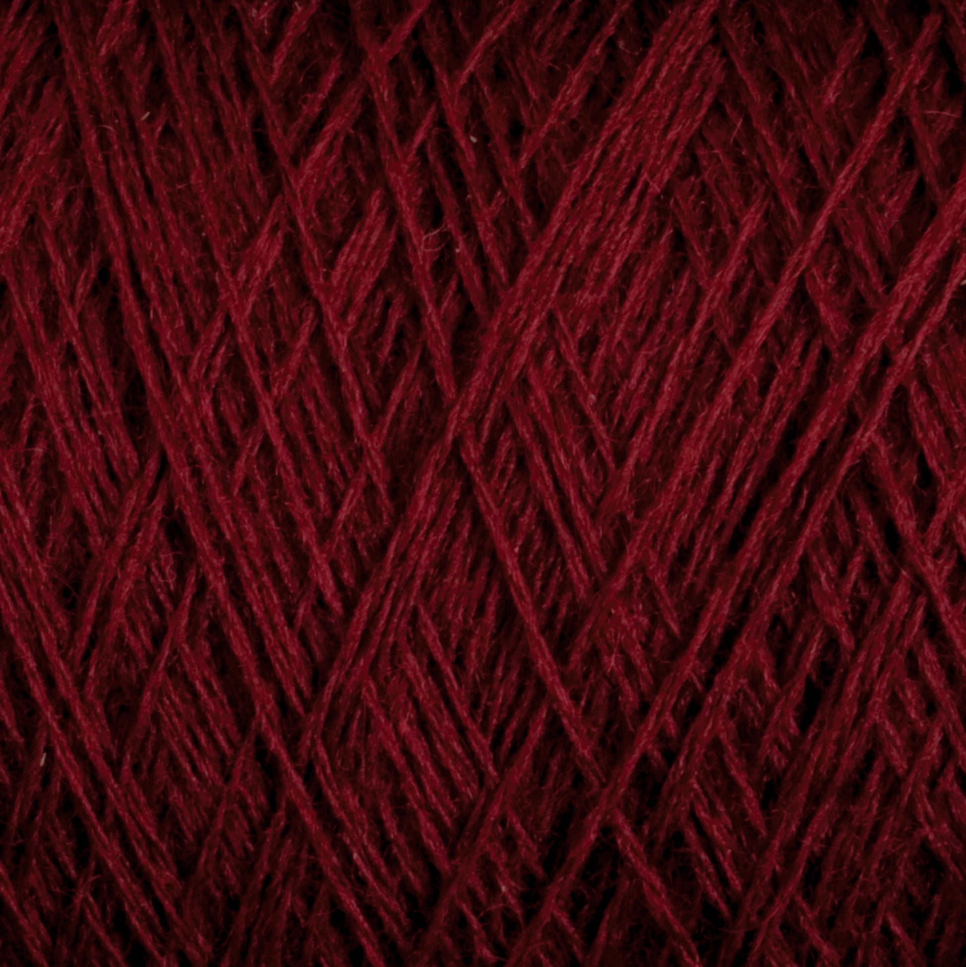 A close-up image of dark red JaggerSpun Superfine Merino 2/18 Yarn by Jagger Brothers, Inc., featuring intricate overlapping strands. The texture appears soft and slightly fuzzy, showcasing the fine details of the individual fibers twisted together, perfect for hand knitters.