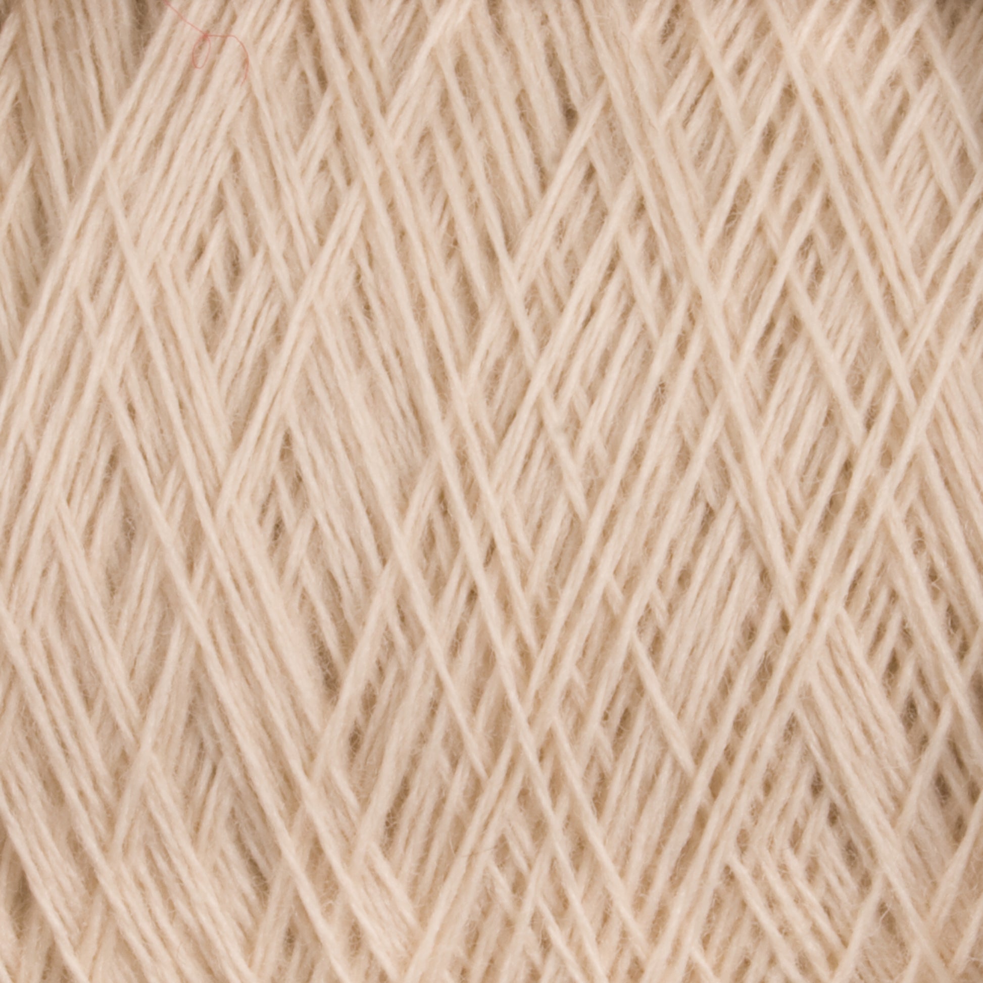 Close-up of a ball of cream-colored, worsted weight yarn with intricate crisscrossing threads. The fine texture and soft tone suggest it may be made from merino wool, specifically JaggerSpun Superfine Merino 2/18 Yarn in a large cone by Jagger Brothers, Inc., commonly favored by hand knitters for knitting and crocheting.