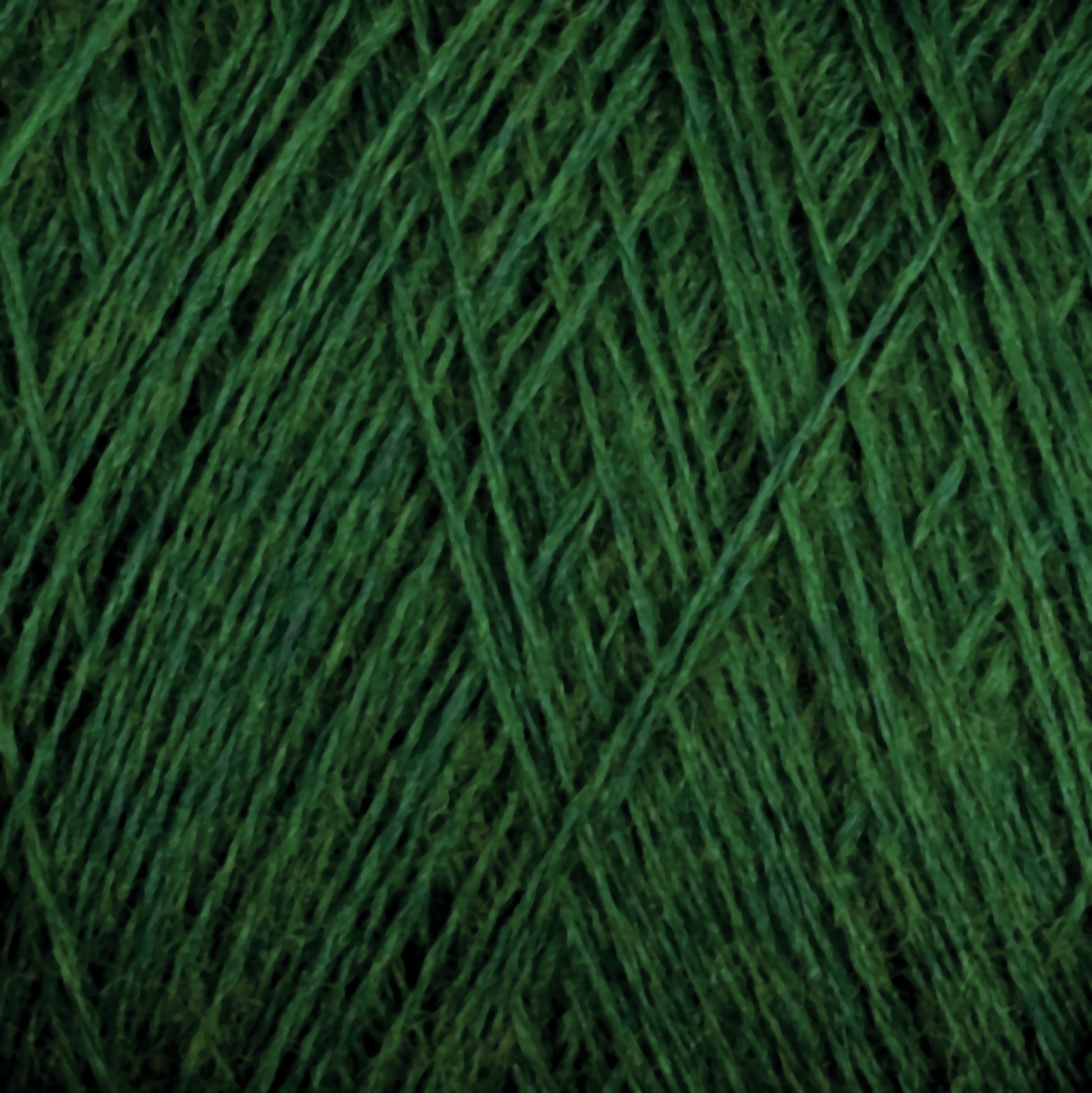 Close-up image of JaggerSpun Superfine Merino 2/18 Yarn from Jagger Brothers, Inc., in green, tightly wound. The texture of the Merino wool fibers is slightly coarse with varying shades of green, giving it a rich and textured appearance. The hand knitters' yarn strands are intertwined to form neat, parallel lines across the image.