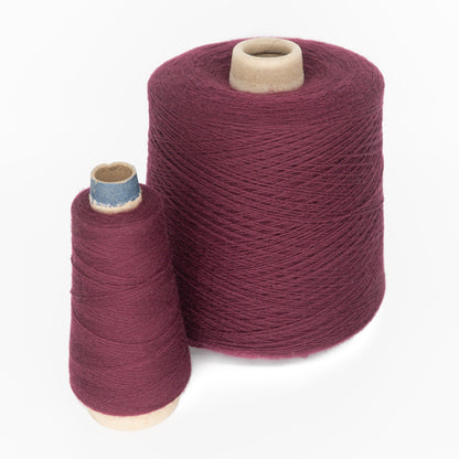 Two spools of maroon-colored Merino wool yarn are shown. The larger spool, a JaggerSpun Superfine Merino 2/18 Yarn Large Cone by Jagger Brothers, Inc., is almost double the height and width of the smaller spool. Both spools are placed upright on a white background.