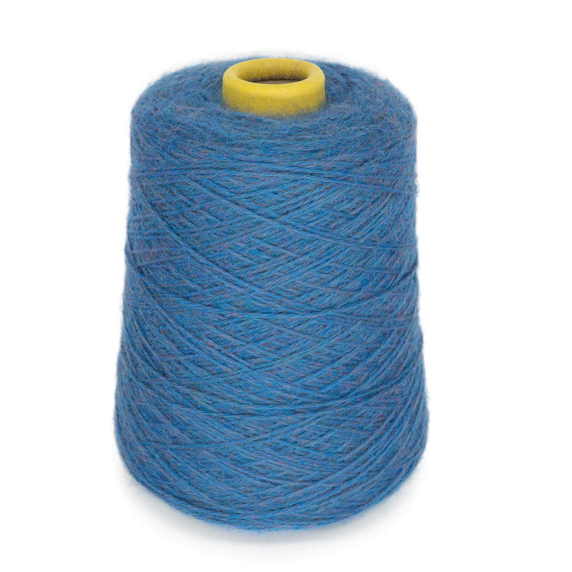 The JaggerSpun Heather 3/8 by Jagger Brothers, Inc. is showcased against a white background, featuring a large spool with yarns exhibiting a slightly fuzzy texture and a rich, vibrant blue color. The yarn is wound neatly in concentric layers around a yellow core.