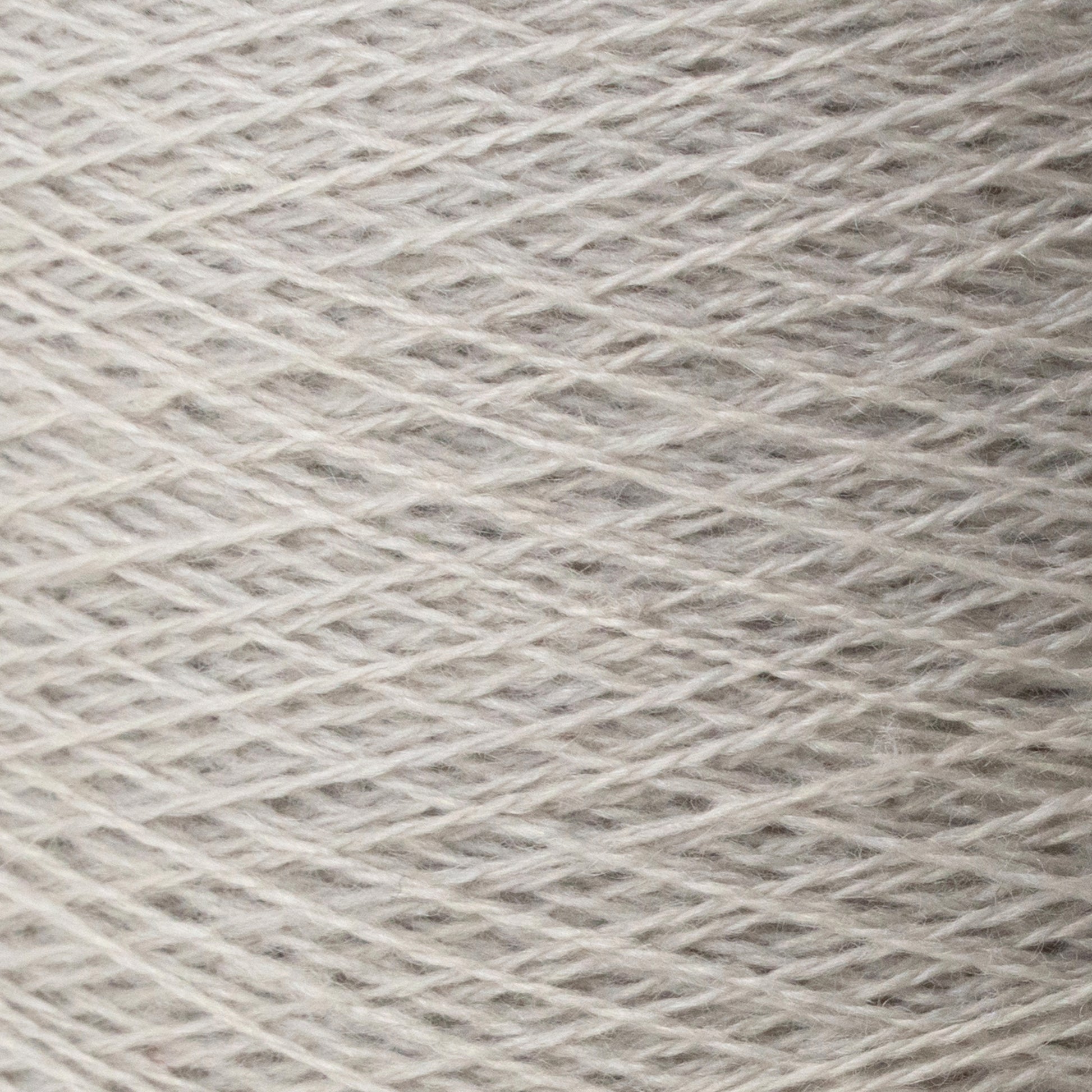 Close-up image of a spool of Jagger Brothers, Inc.'s JaggerSpun Zephyr Wool-Silk 2/18 Yarn in light gray. The fibers, made from luxurious Australian merino wool blended with silk, are tightly wound in a crisscross pattern, showcasing the texture and slight variations in color.