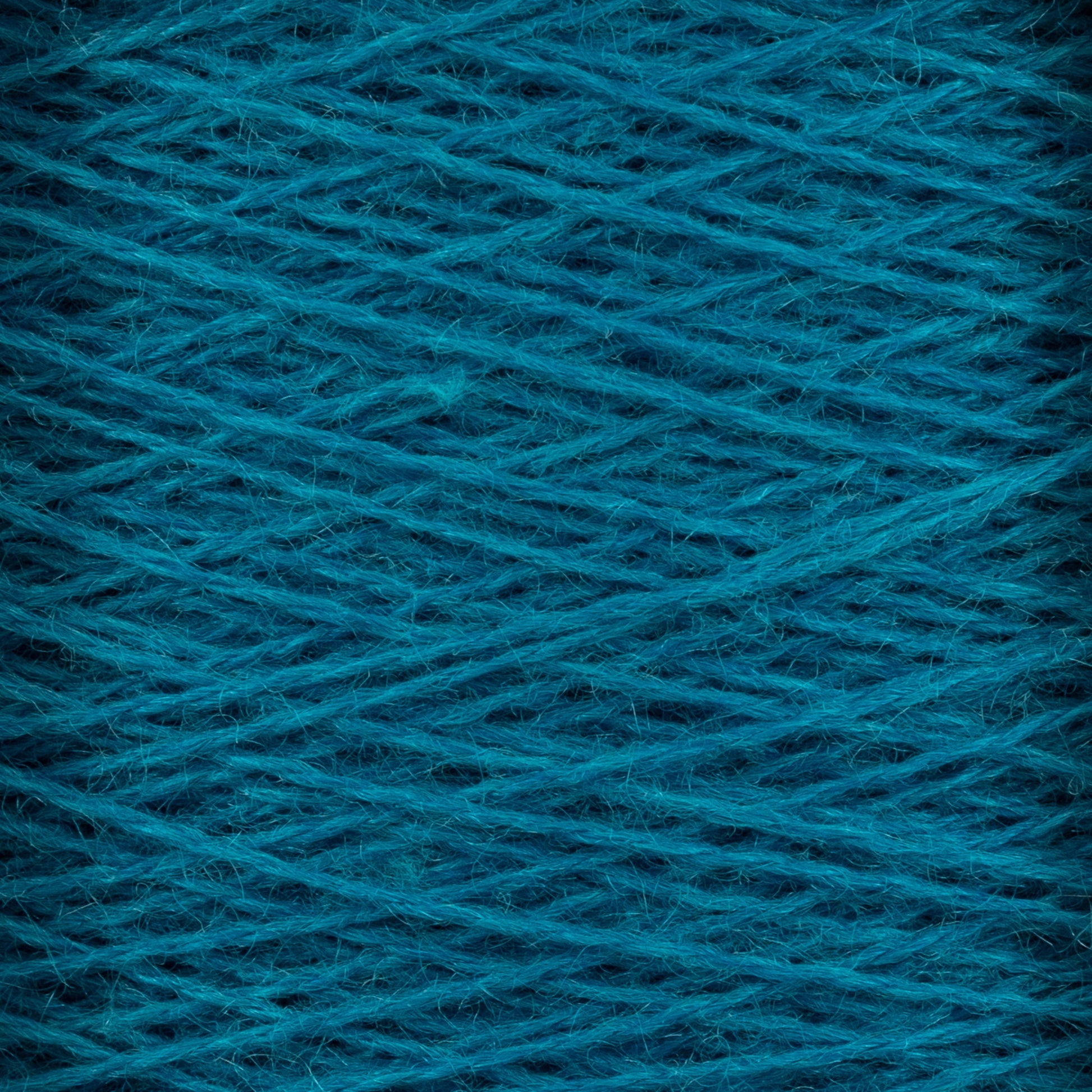 Close-up view of a large cone of JaggerSpun Zephyr Wool-Silk 2/18 Yarn by Jagger Brothers, Inc., showcasing its tightly wound dark teal threads in a criss-cross pattern. The texture appears slightly fuzzy, hinting at the softness of the material. This luxurious yarn boasts vibrant, rich colors that enhance its premium silk-like appeal.