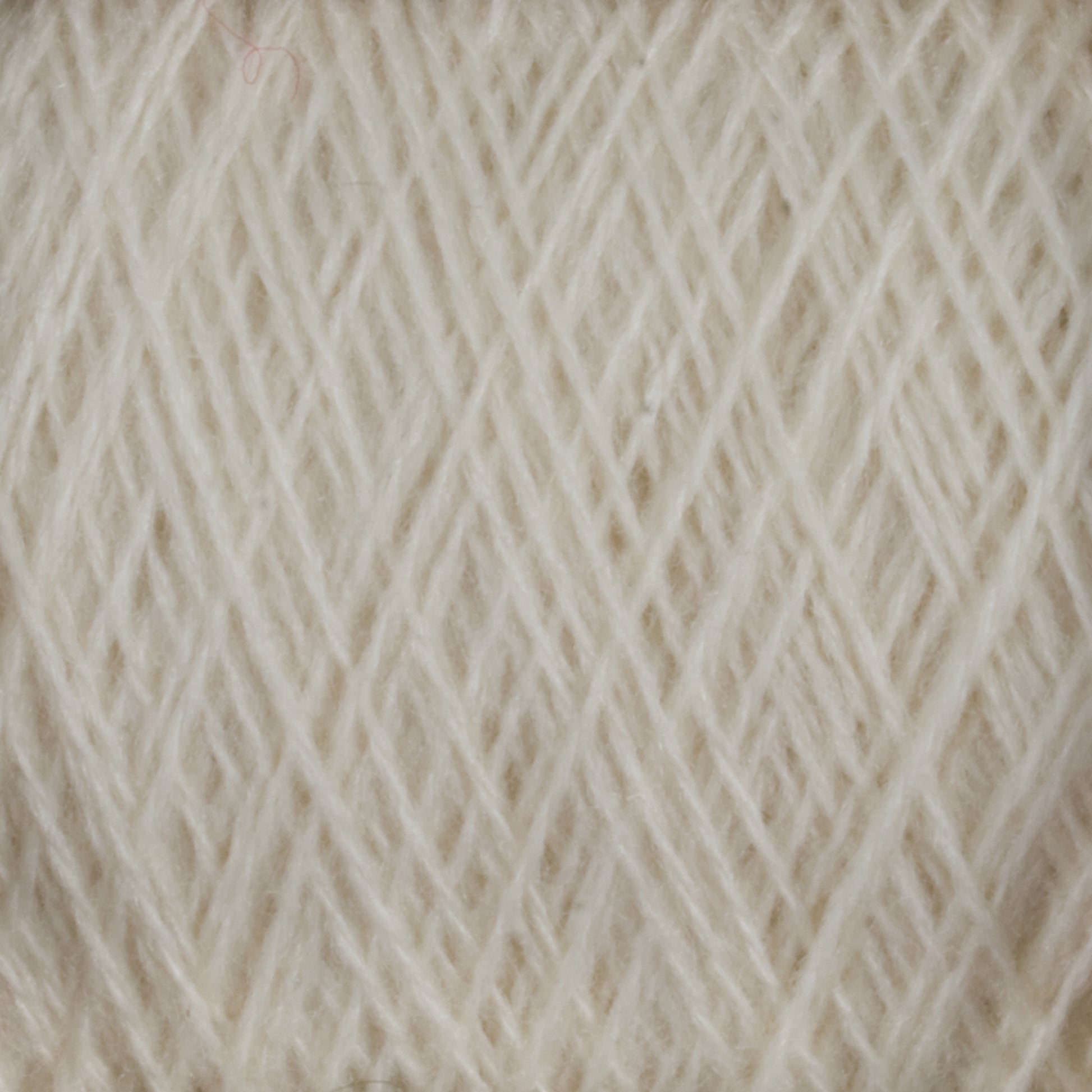 A close-up image of JaggerSpun Zephyr Wool-Silk 2/18 Yarn | Large Cone by Jagger Brothers, Inc., showcasing off-white, luxurious yarn tightly wound in a neat pattern. The individual fibers are visible, creating a textured, soft appearance. Crafted from premium silk and wool, the yarn is arranged in a way that creates a subtle crisscross design.