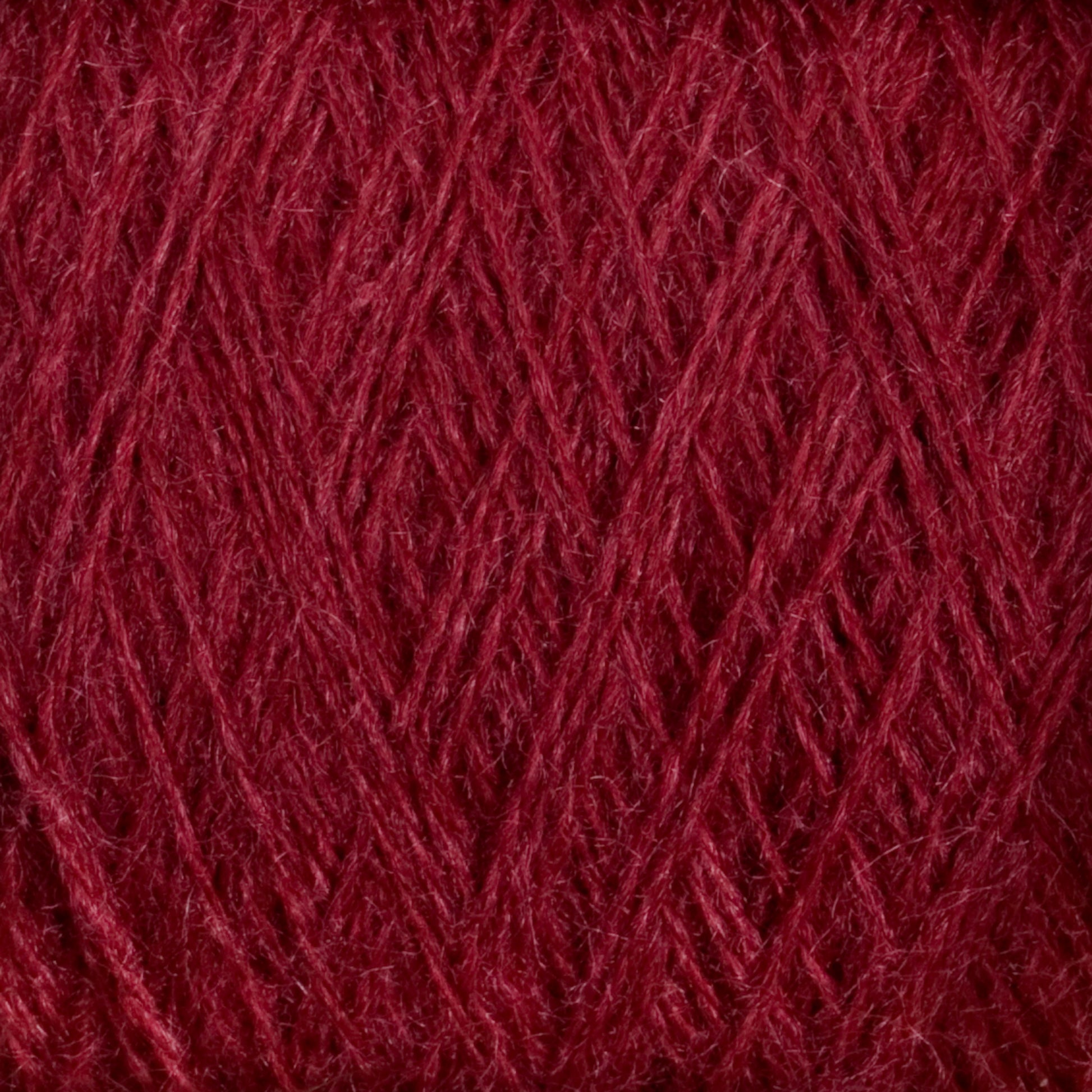 Close-up of a ball of deep red, luxurious JaggerSpun Zephyr Wool-Silk 2/18 Yarn from Jagger Brothers, Inc. The fibers are tightly wound, and the texture appears soft and fuzzy with a rich and vibrant color. The intricate crisscrossing pattern of the strands is visible, showcasing the yarn's consistent thickness and evenness, reminiscent of premium silk.